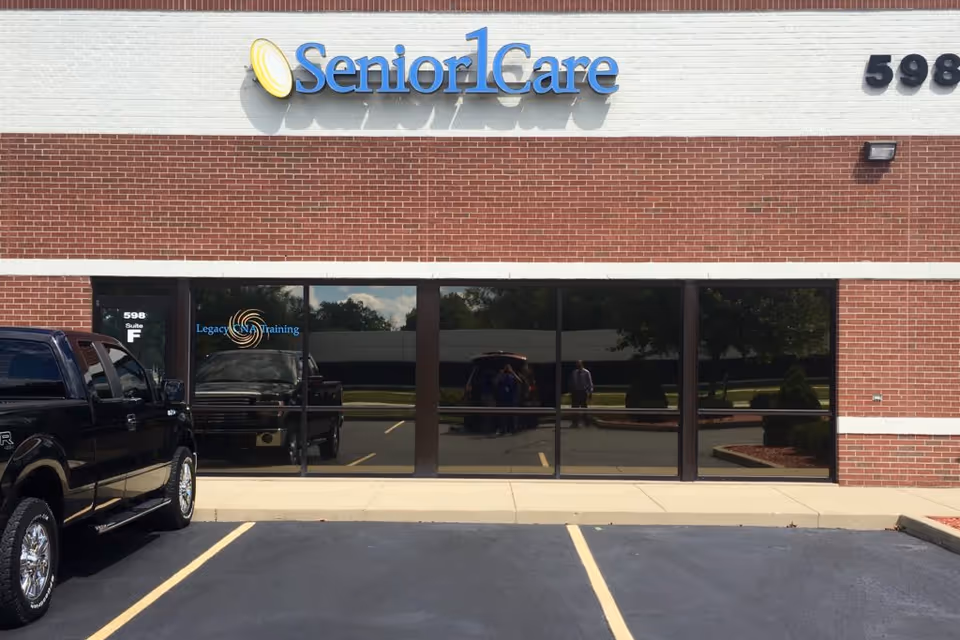 Exterior view of a SeniorCare facility with brick facade, glass entrance, and parking.