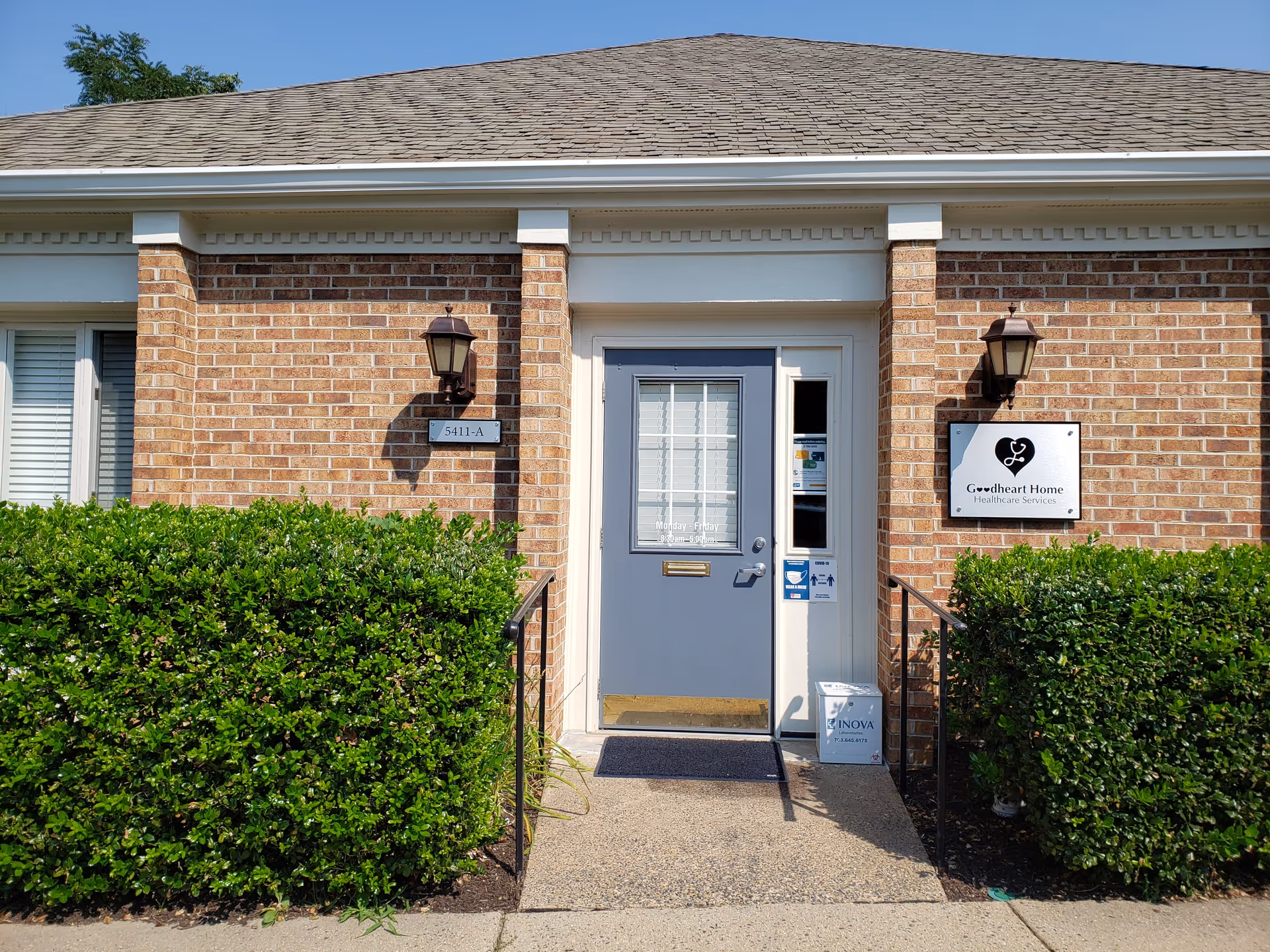 Brick building front with blue door, hedges, and Goodheart Home Healthcare sign.