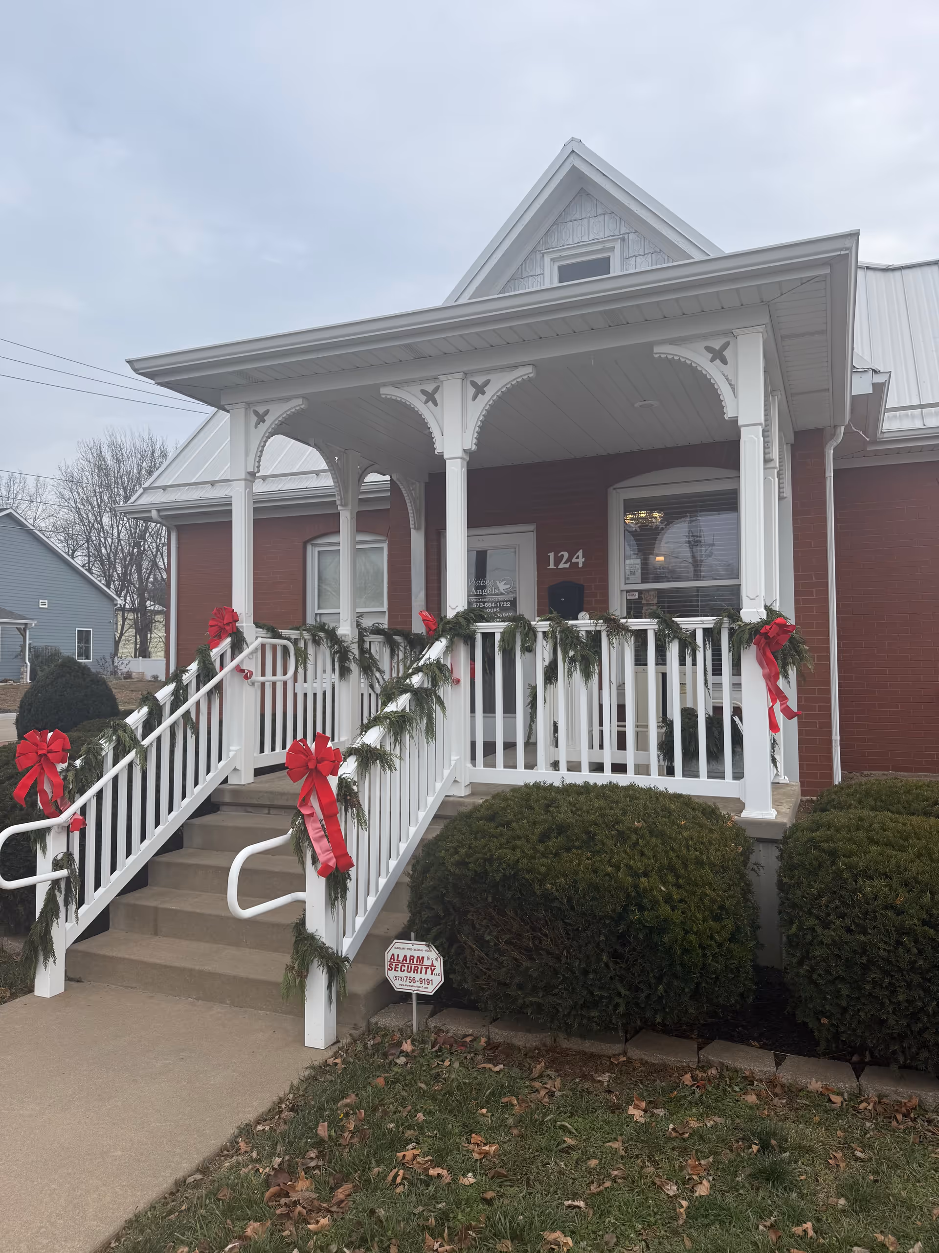 Brick senior home entrance with white porch and festive garlands and red bows