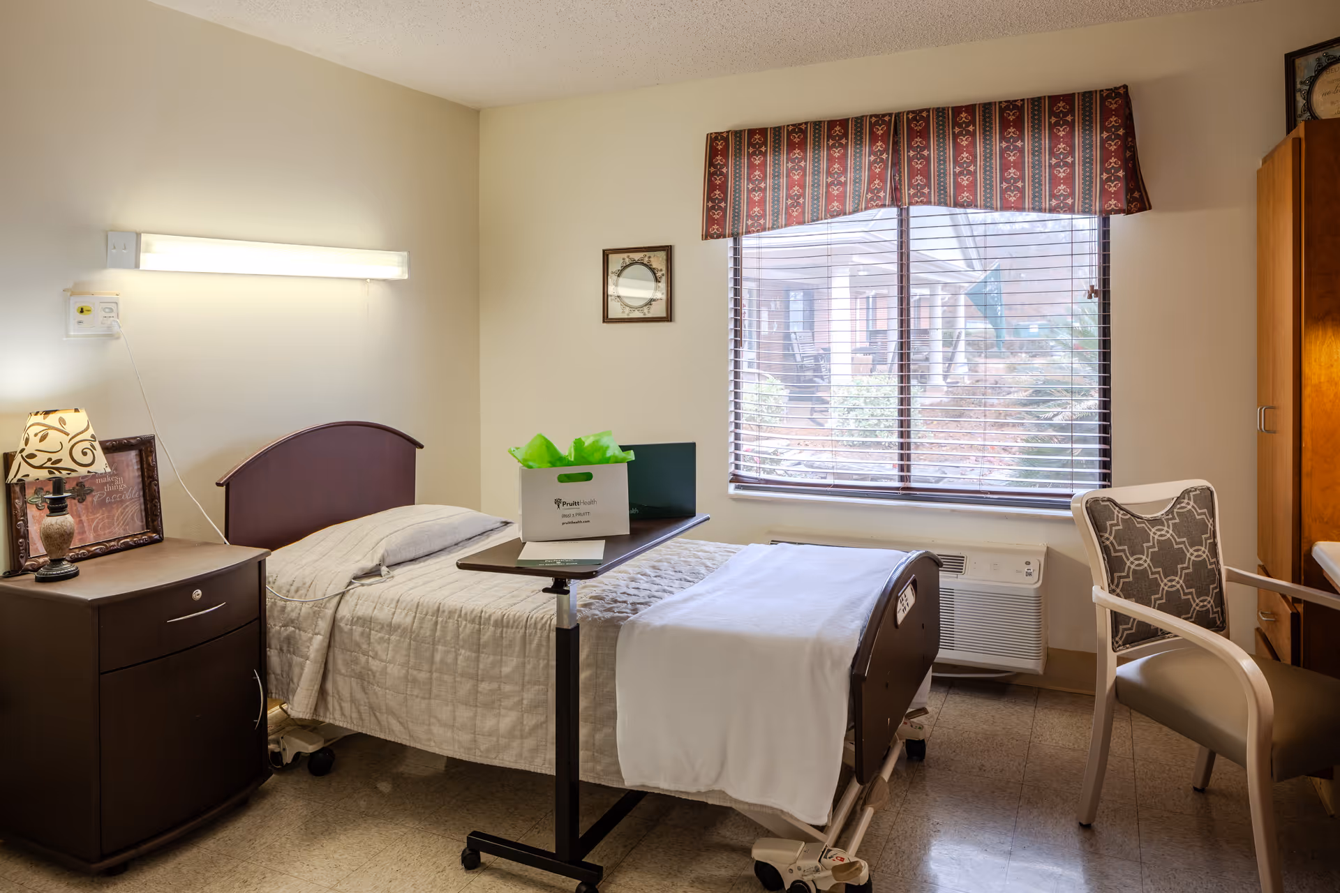Senior living patient bedroom with a hospital bed, nightstand, window, and chair.