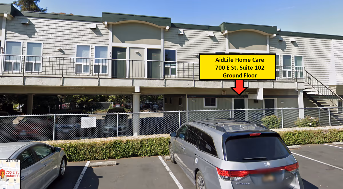 Two-story senior living facility exterior with a yellow AidLife Home Care sign and parked cars.