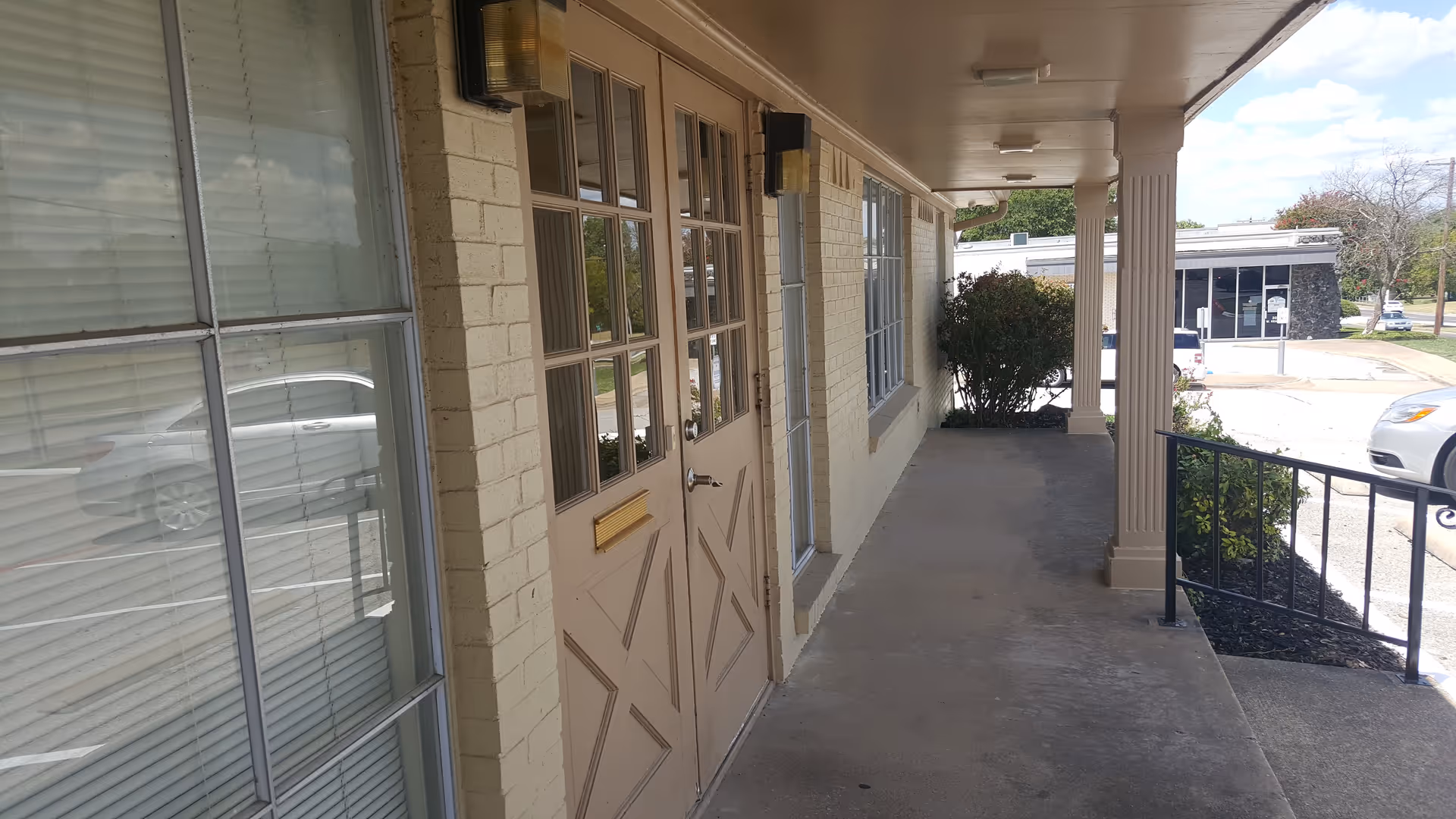 Covered exterior walkway along a beige brick senior care building with doors and windows.