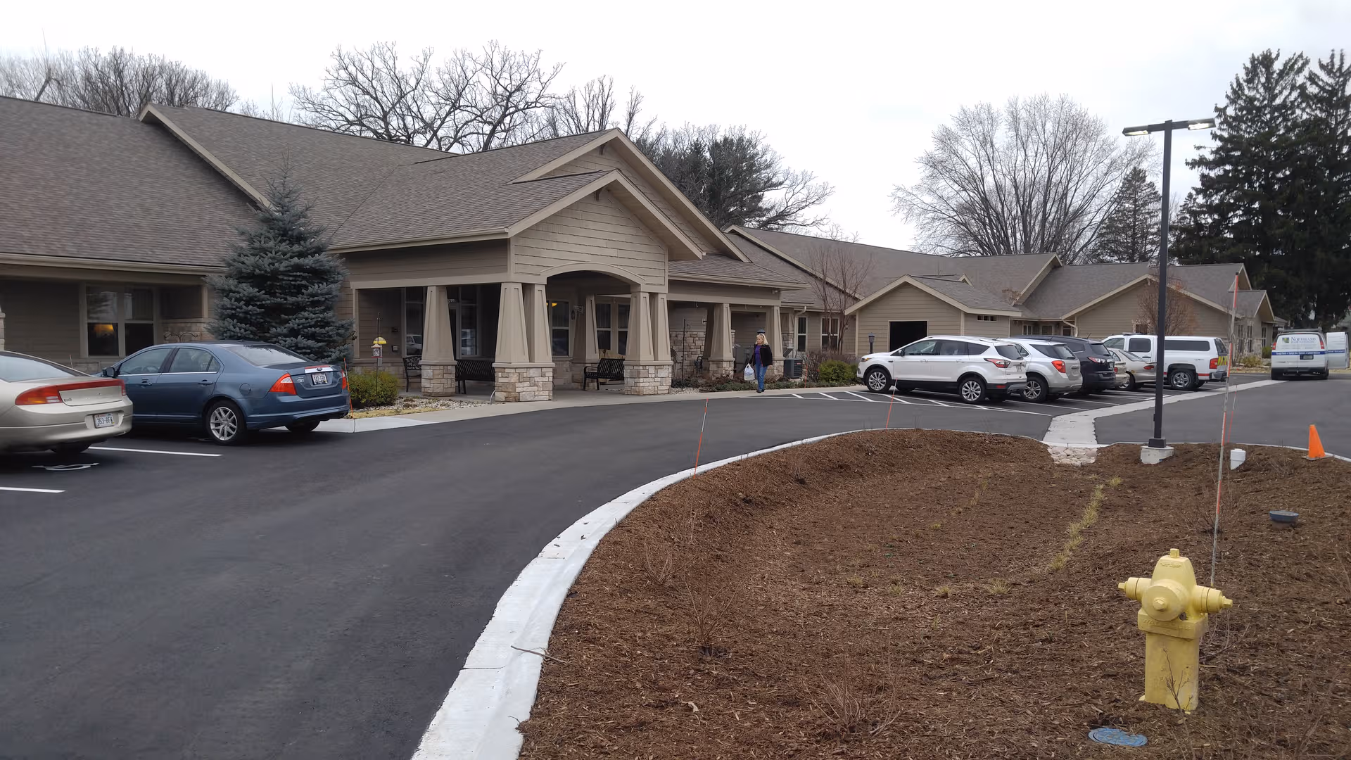 Exterior view of a senior living facility with parked cars and a curved driveway.
