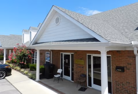Exterior view of Centennial Adultcare Center entrance with brick facade, white columns, and signage.