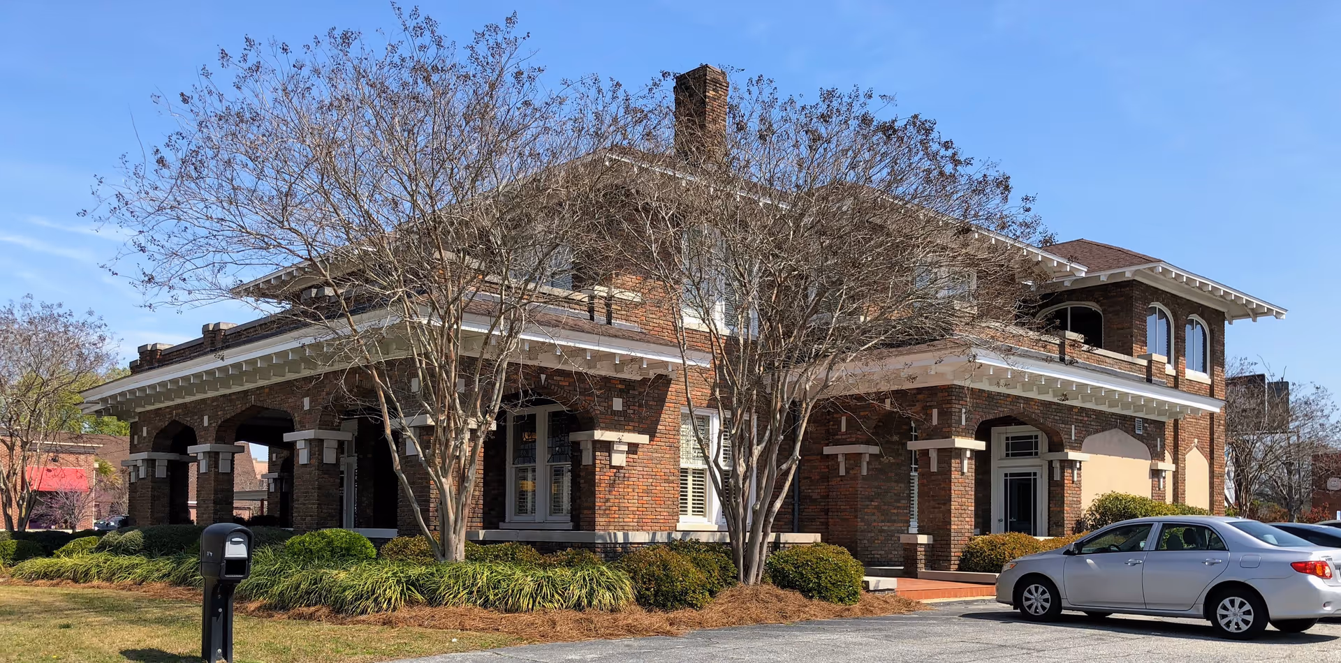 Brick senior living facility exterior with arches, landscaping, and a parked car.