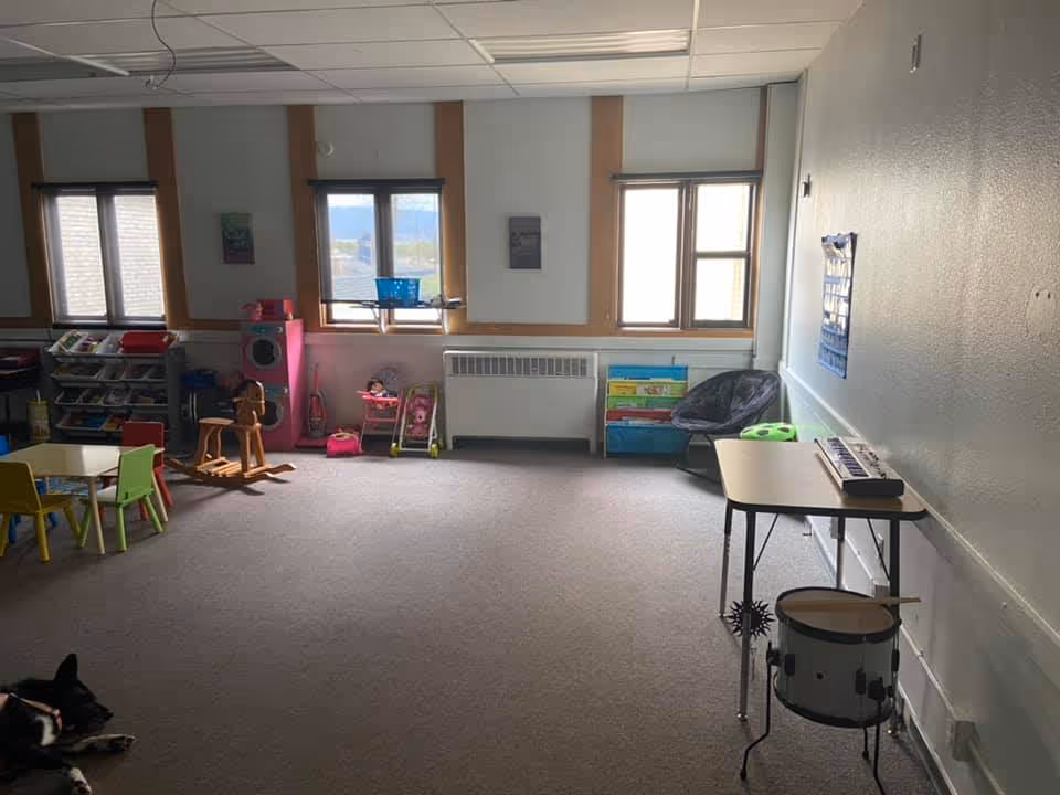 A children's playroom with toy shelves, tables, chairs, and a drum set.