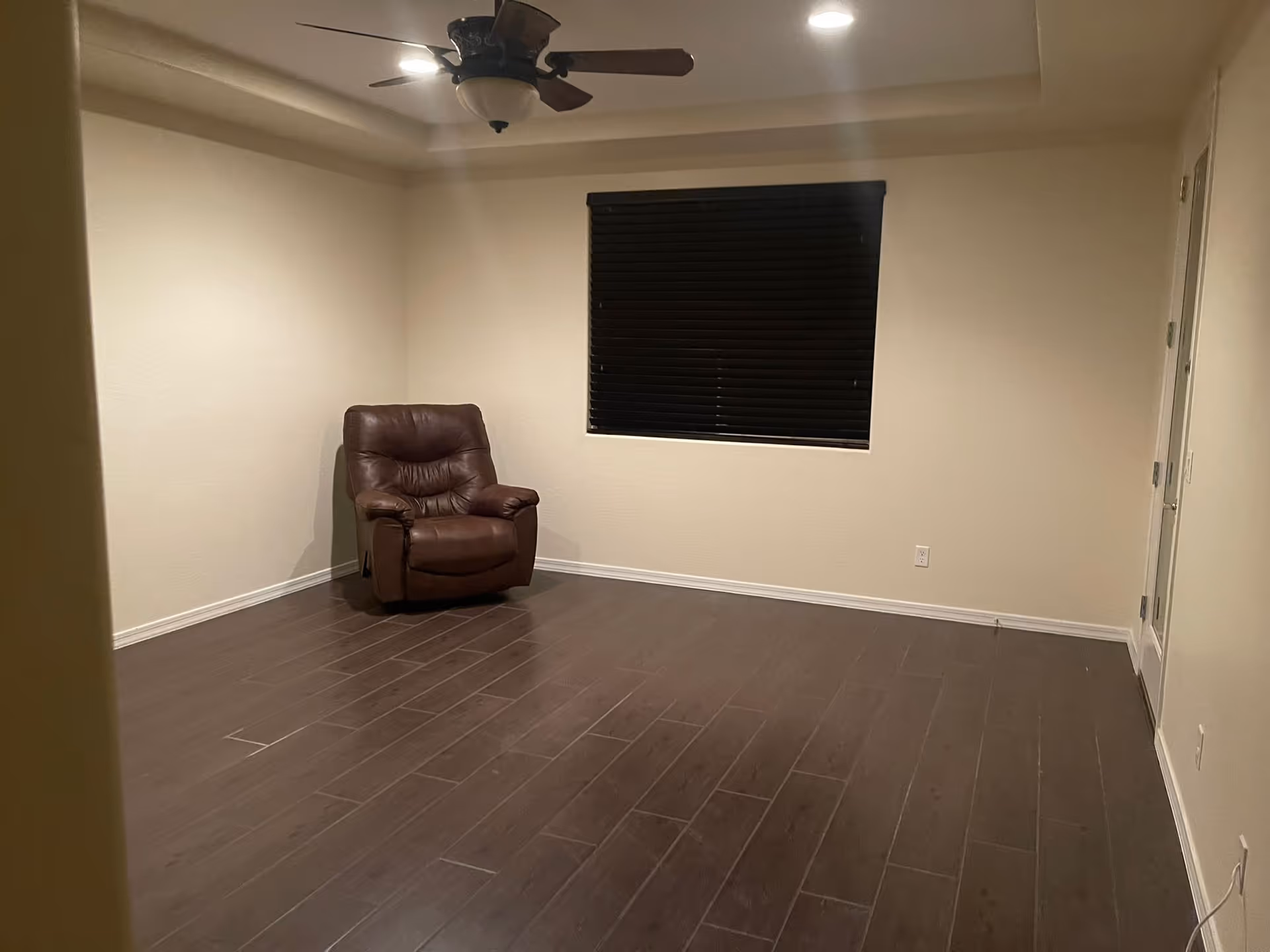 Empty living room with brown recliner, window blinds, and a ceiling fan.
