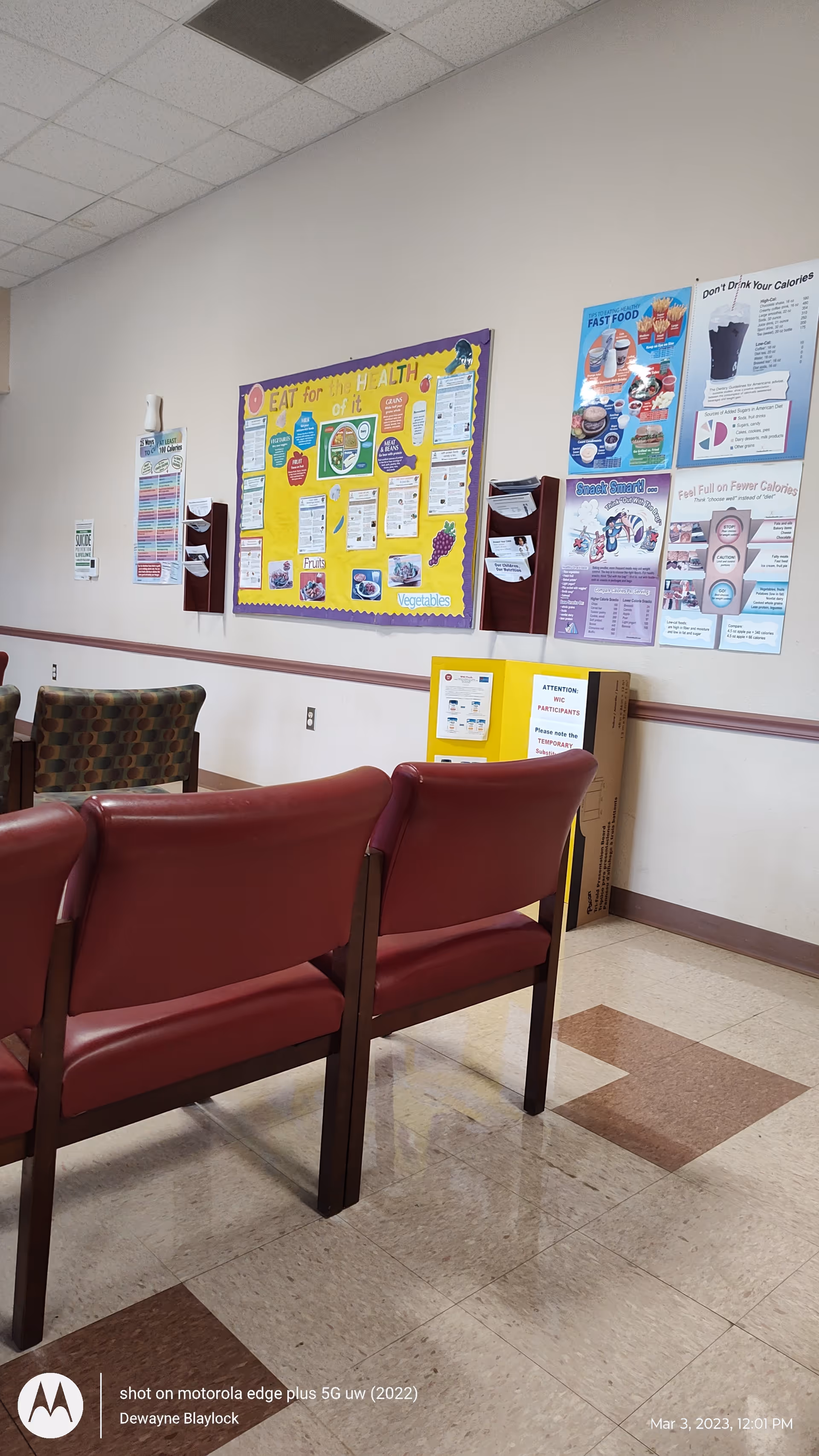 Empty waiting area with maroon chairs and health information posters on the wall.