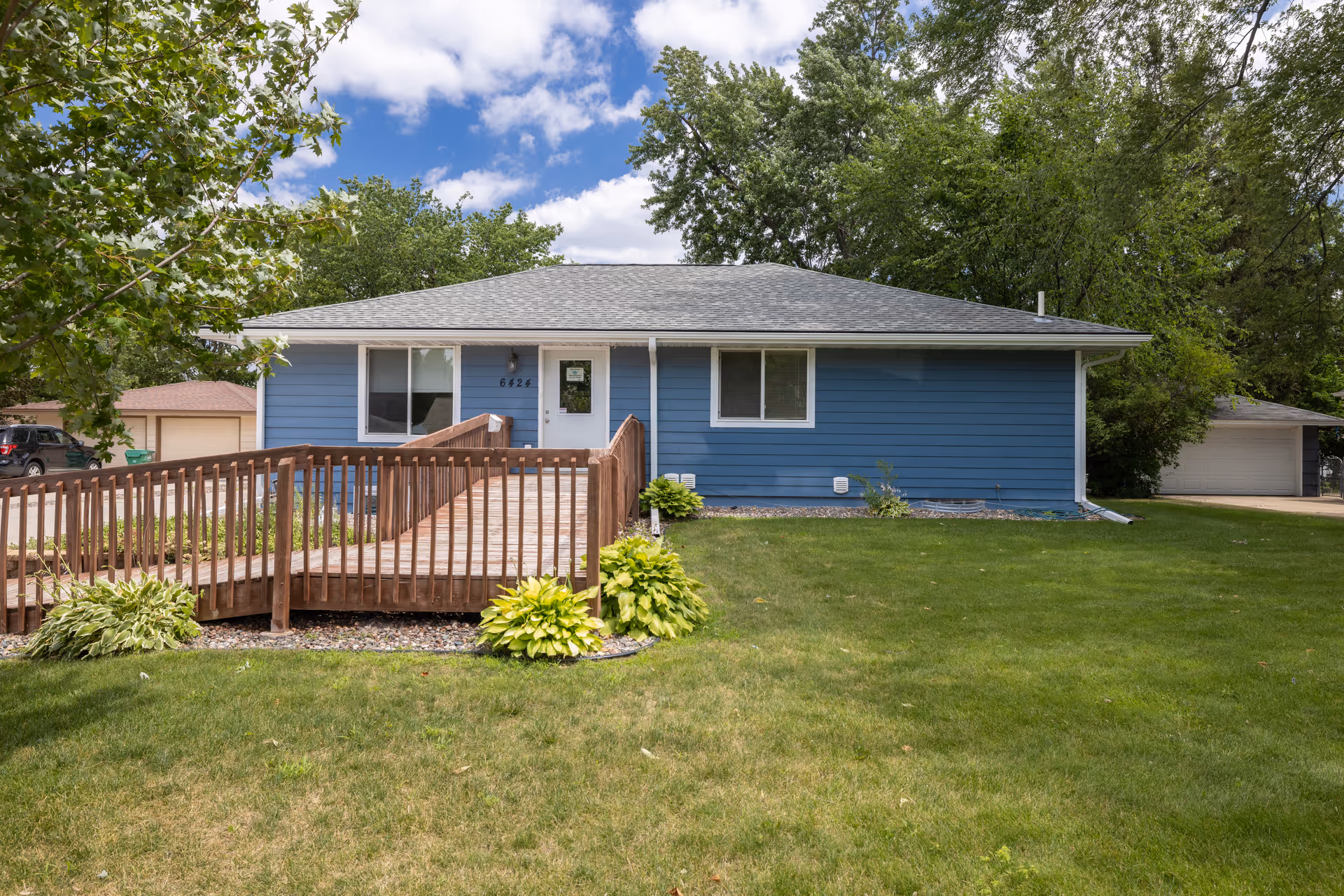 Blue single-story home with wooden ramp to the front door and well-kept lawn.