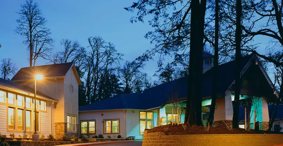 Twilight exterior of The Pearl At Kruse Way with lit windows and trees surrounding the entrance.
