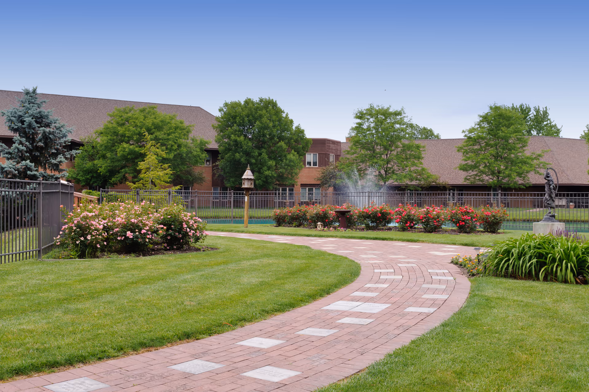 Outdoor courtyard of Hospice of Northwest Ohio with brick path, rose beds, fountain, and statue.