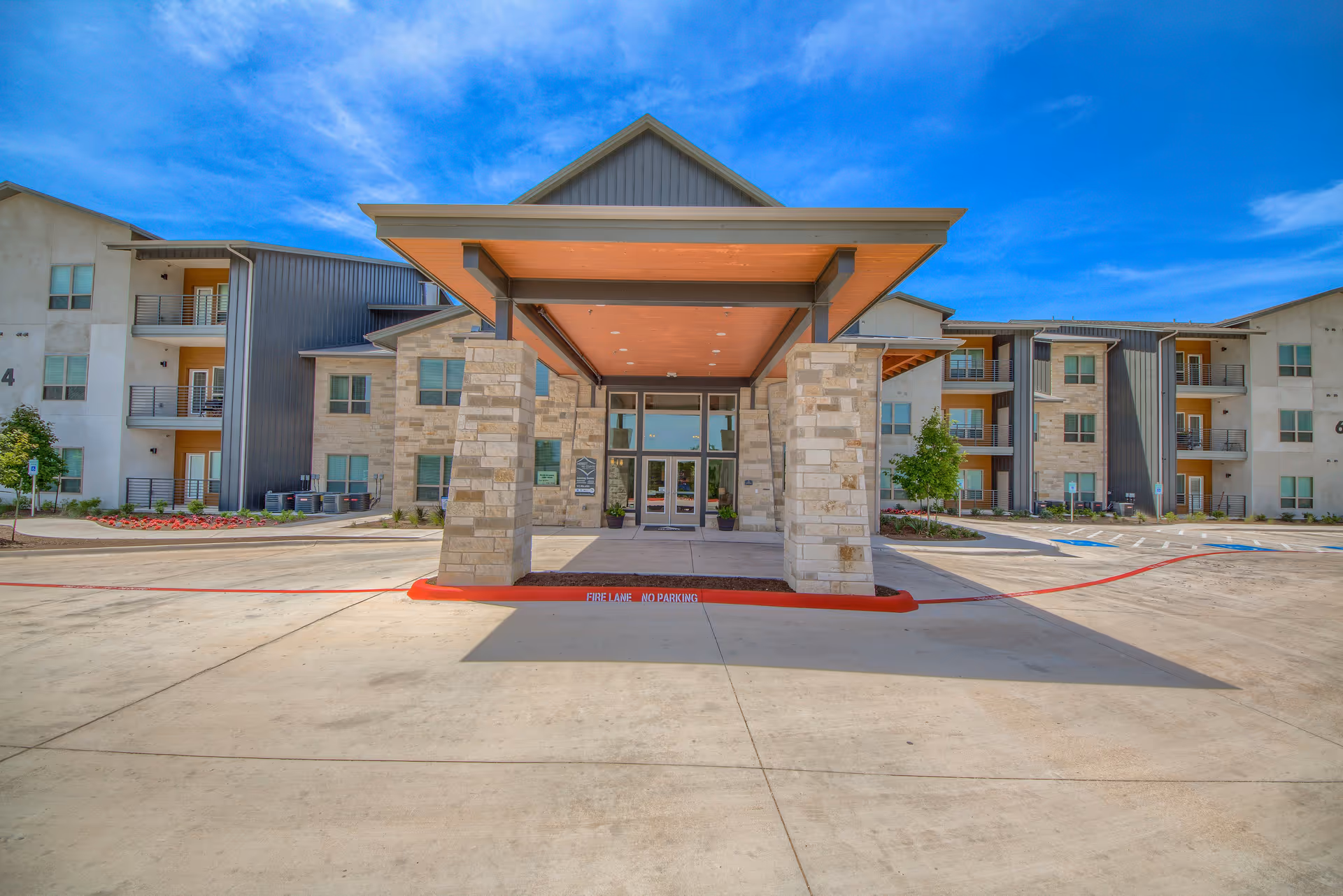 Covered main entrance with stone pillars leading to a modern three-story residential building under a bright blue sky.
