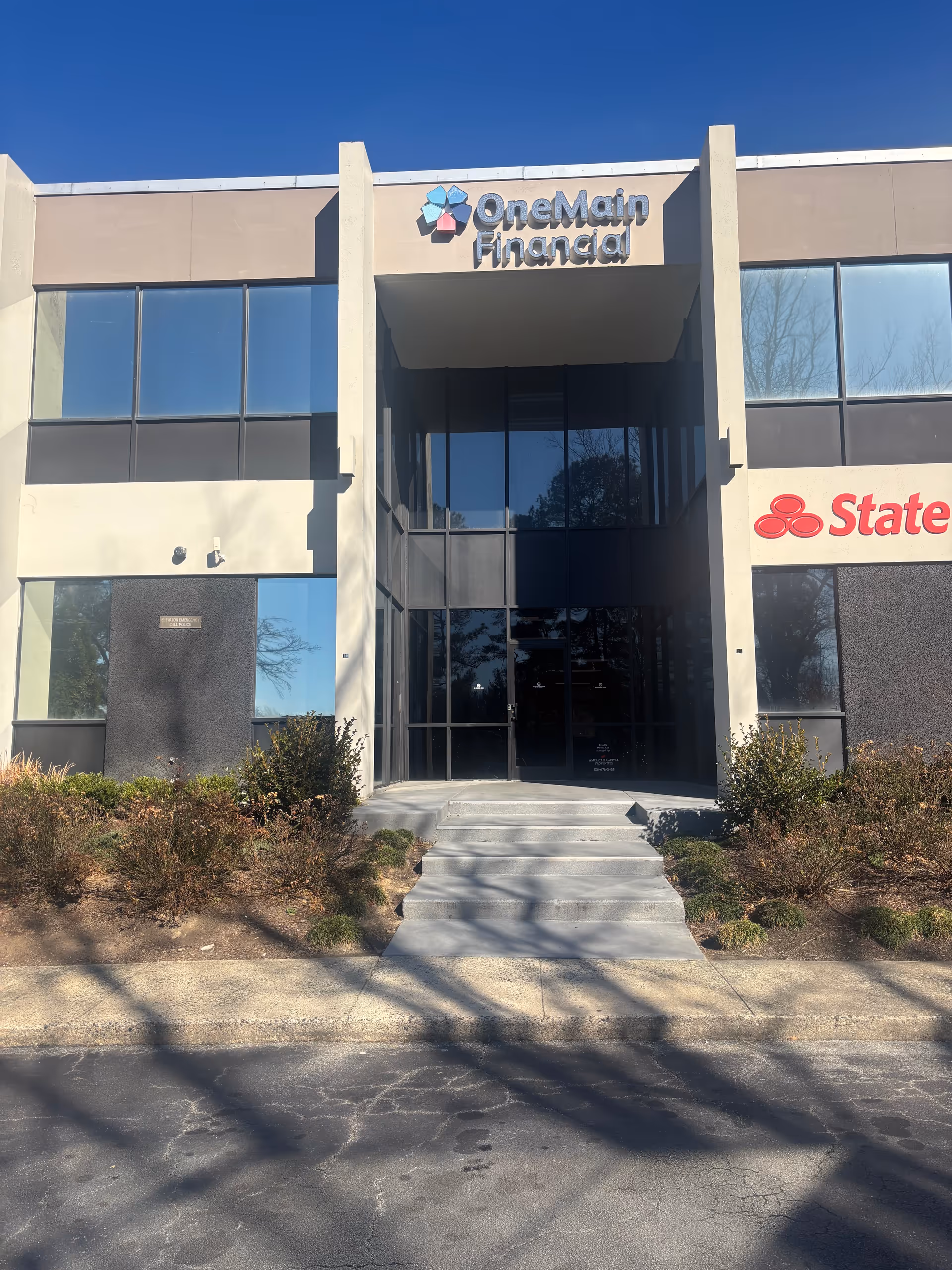 Front of a commercial building with OneMain Financial and State Farm signage, stairs to entrance.