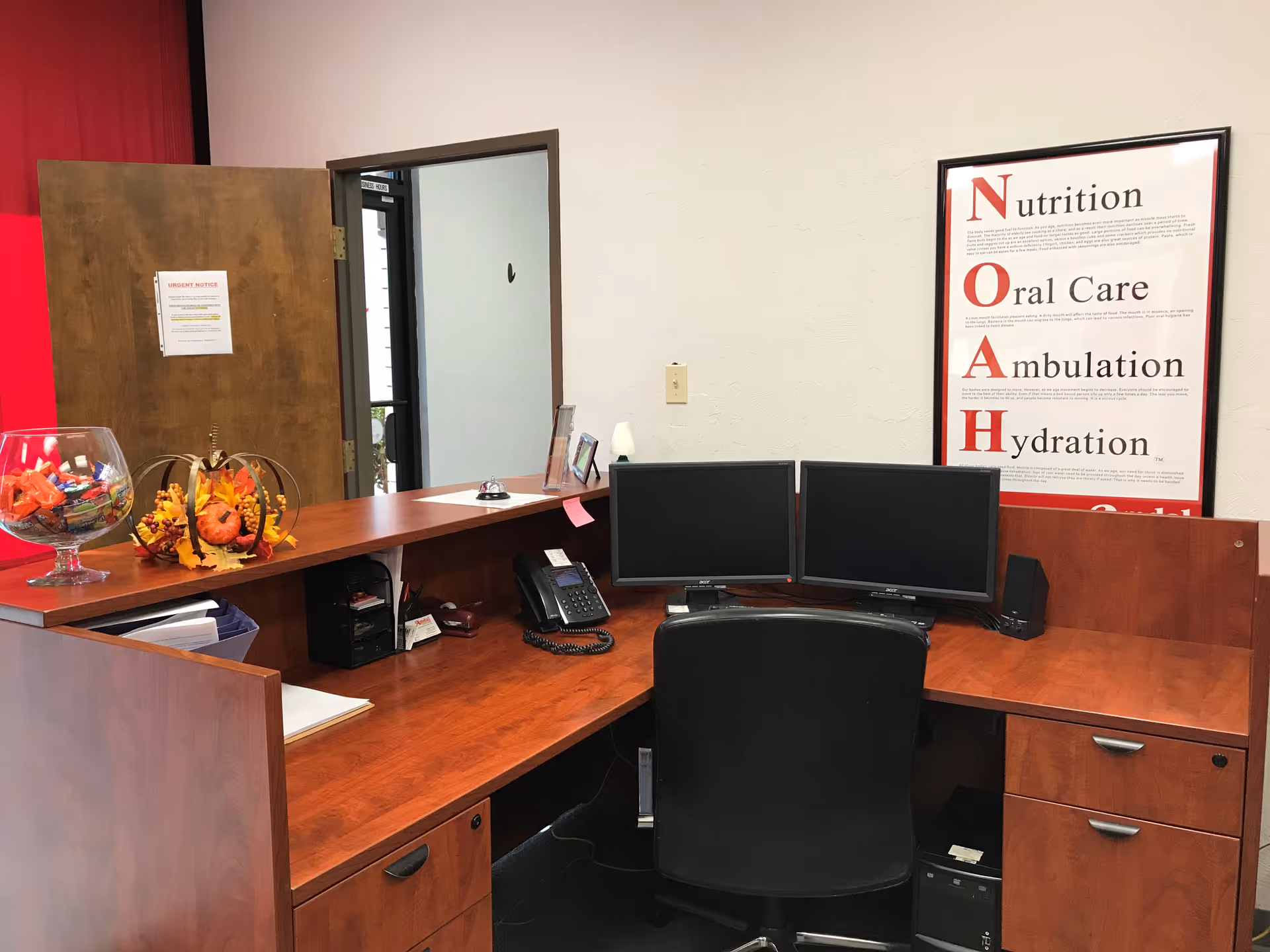 Reception desk with two computer monitors and a NOAH poster on the wall.
