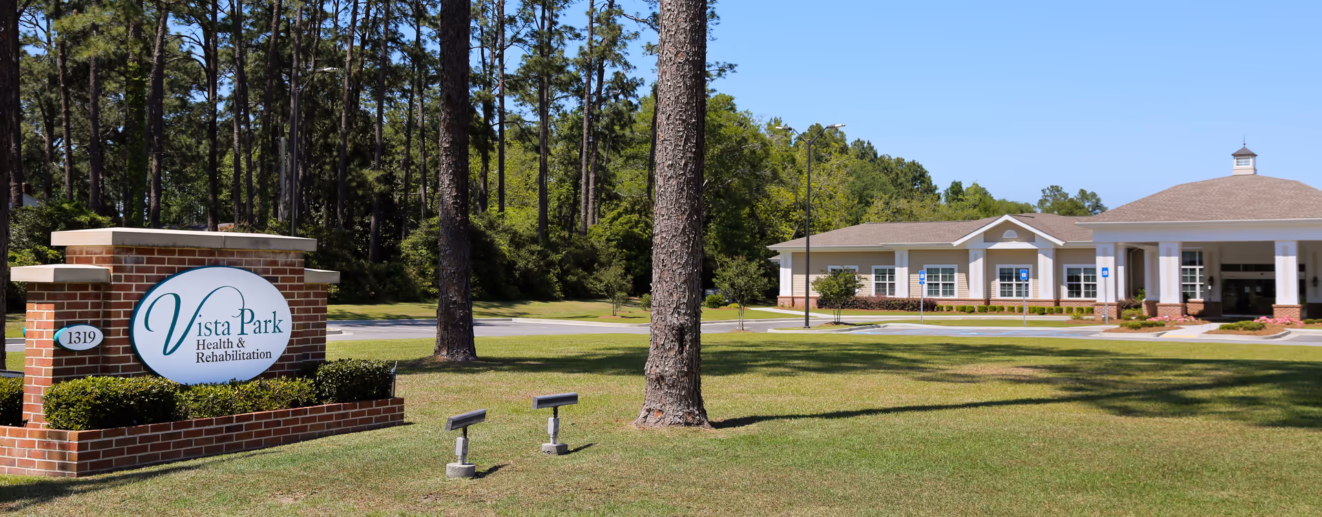 Exterior view of Vista Park Health and Rehabilitation facility with sign and lawn.