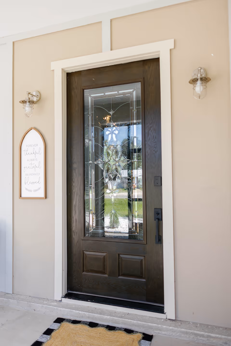 A decorative front door with glass panels, flanked by wall lanterns and a welcome sign.
