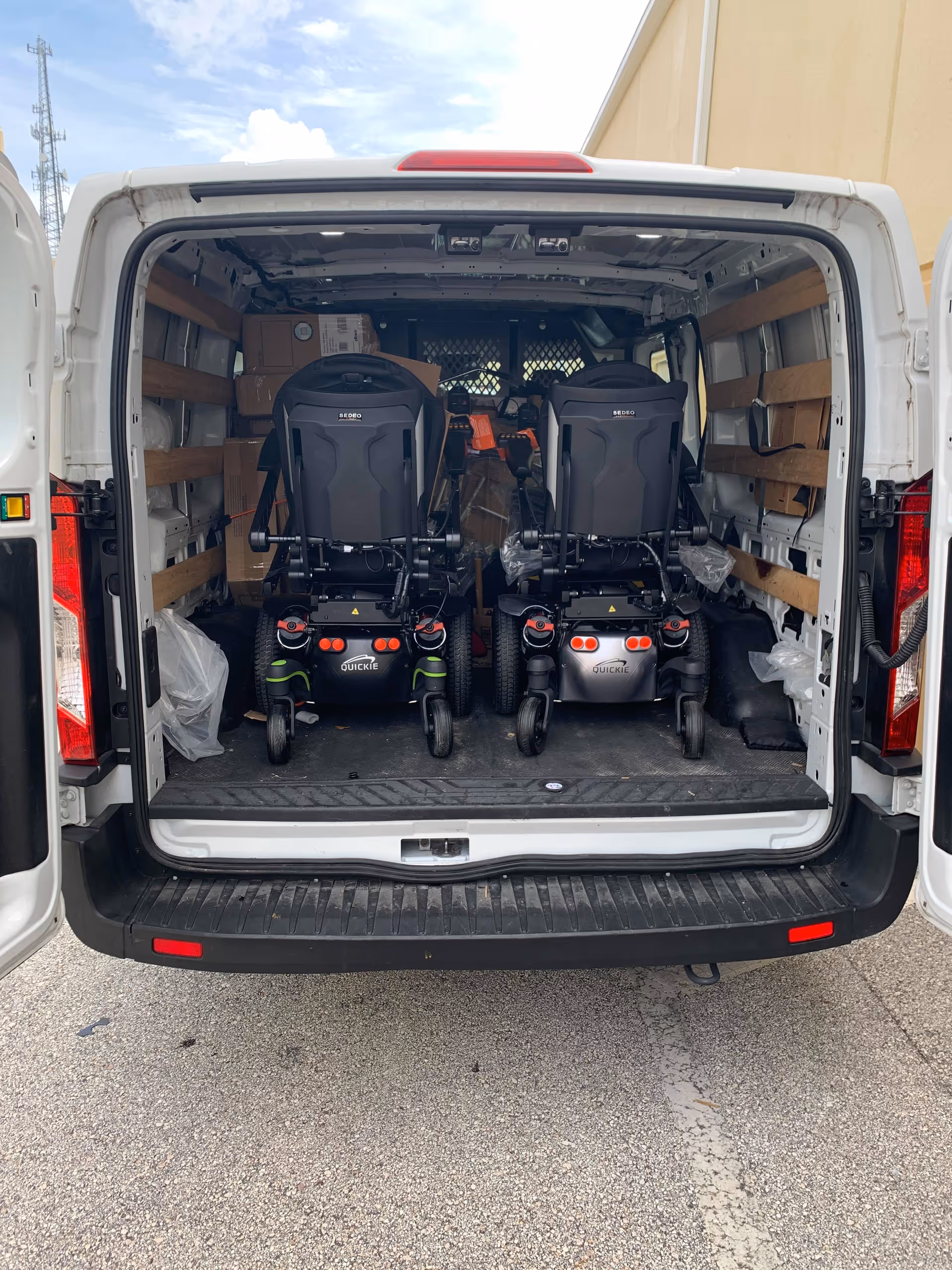 Open back of a white van loaded with two mobility scooters and equipment.