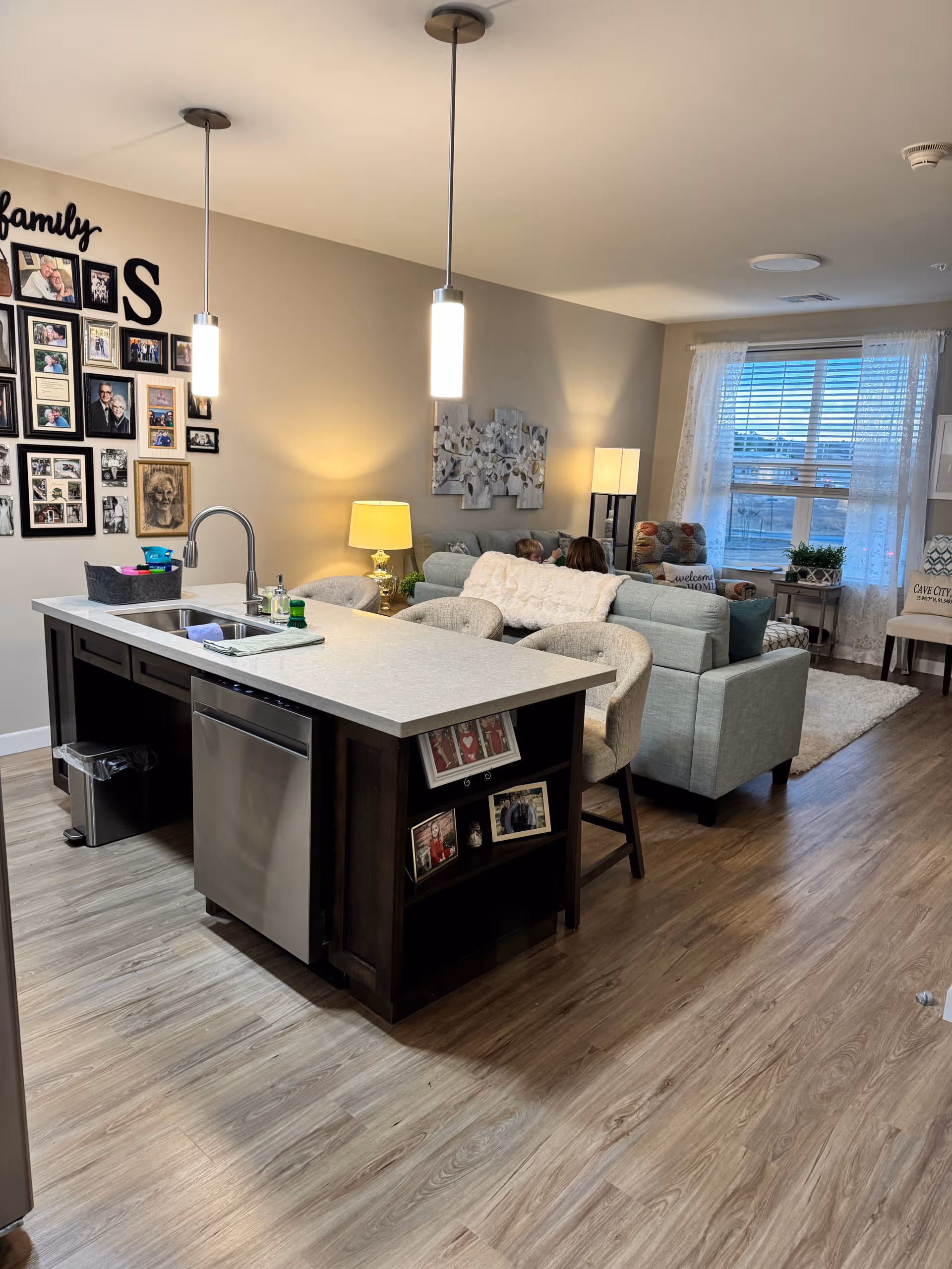 Open-concept living area with a kitchen island, seating, and wall photos at Mira at Maumelle.