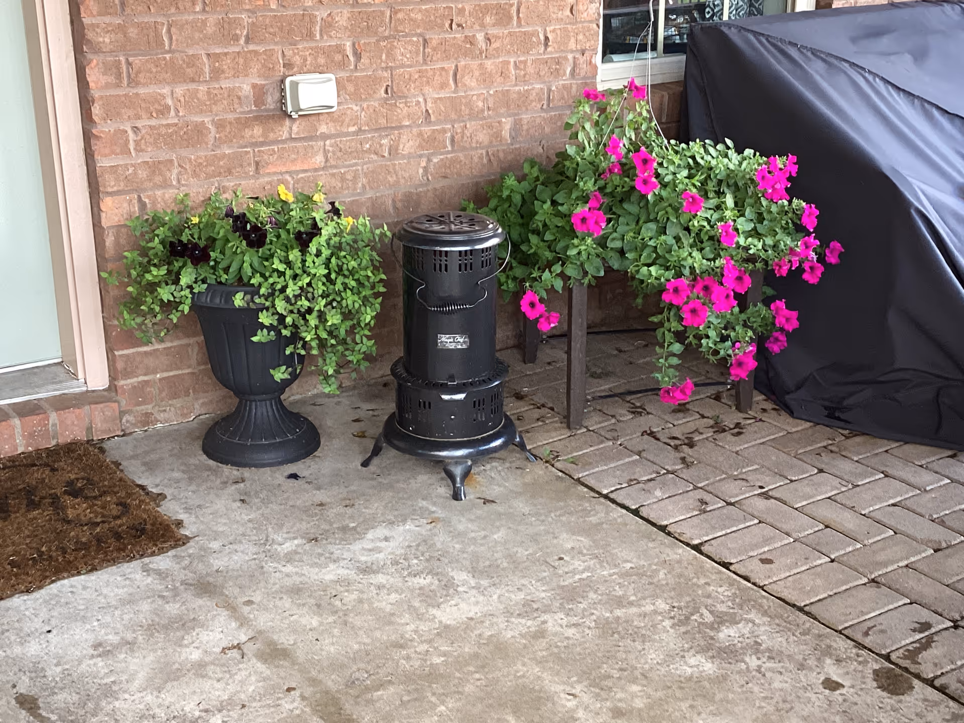 Outdoor patio with brick wall, planters of pink flowers, and a black heater.