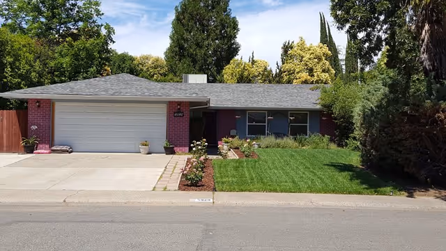 Single-story building exterior with a two-car garage, porch seating, and manicured front lawn.