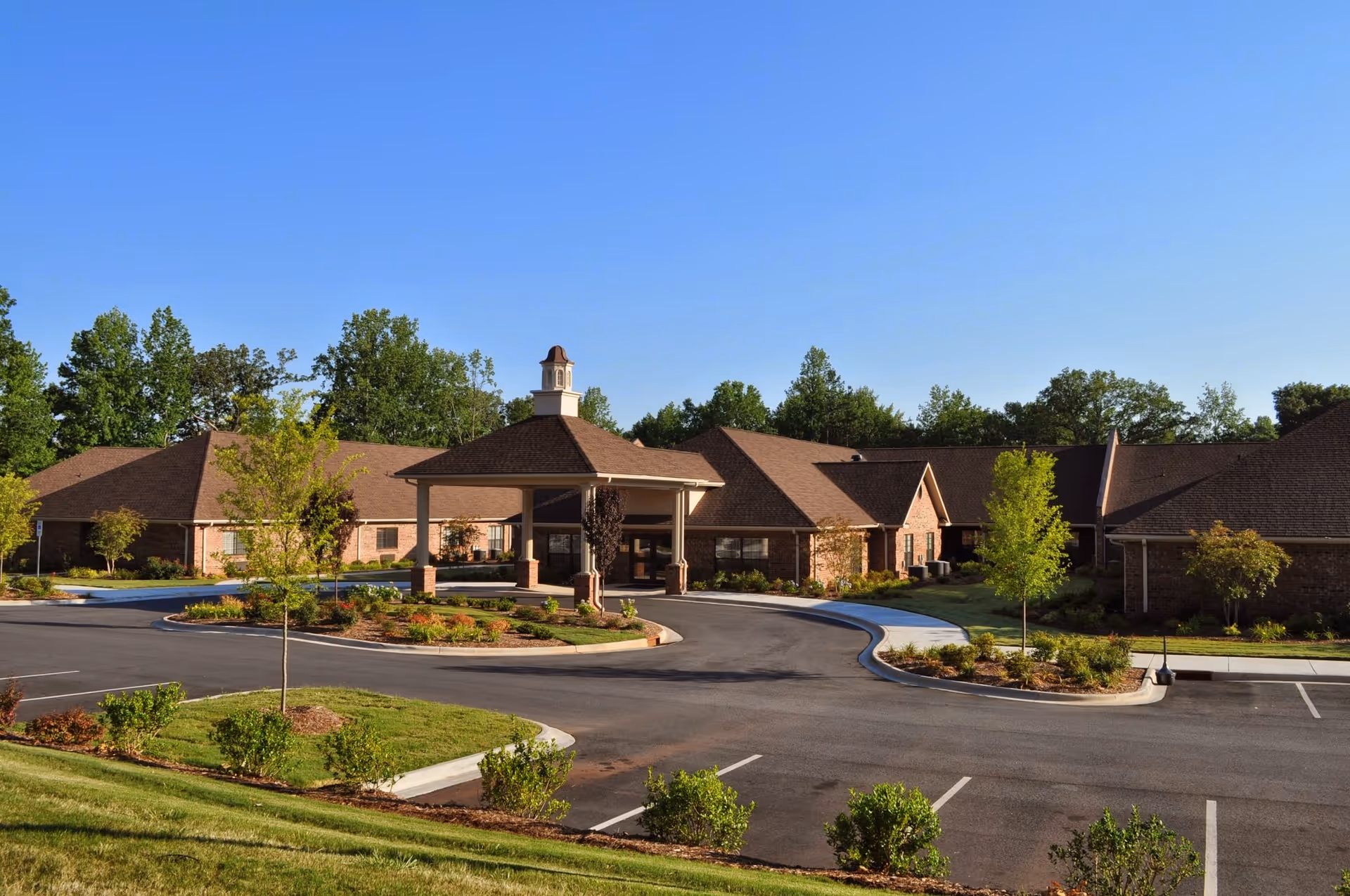 Exterior view of Peak Resources Charlotte facility showing a single-story brick building with a covered entrance, surrounded by landscaped greenery and a parking lot under a clear blue sky.