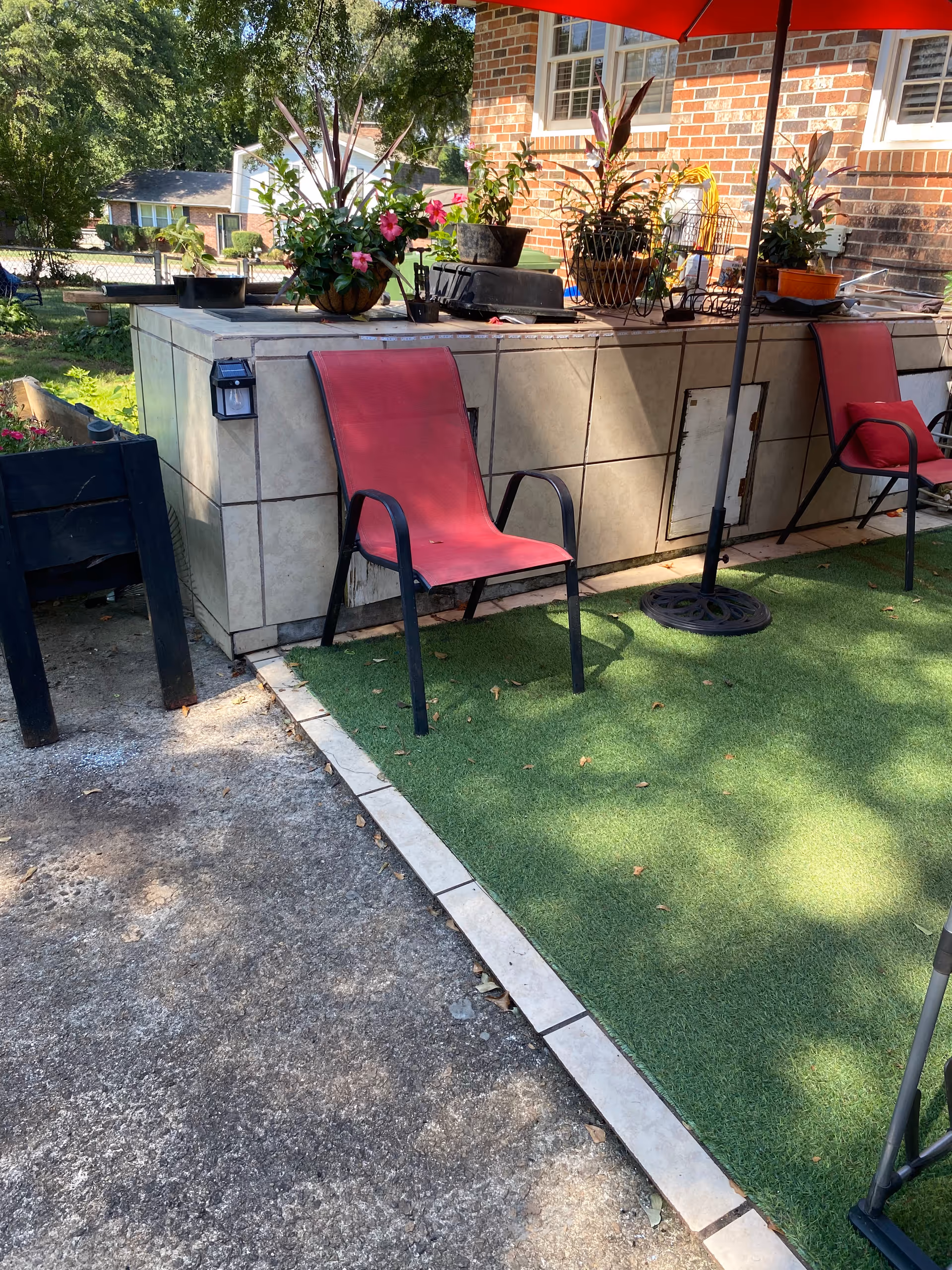 Outdoor patio with pink chairs, potted plants, artificial turf, and a brick building in the background.