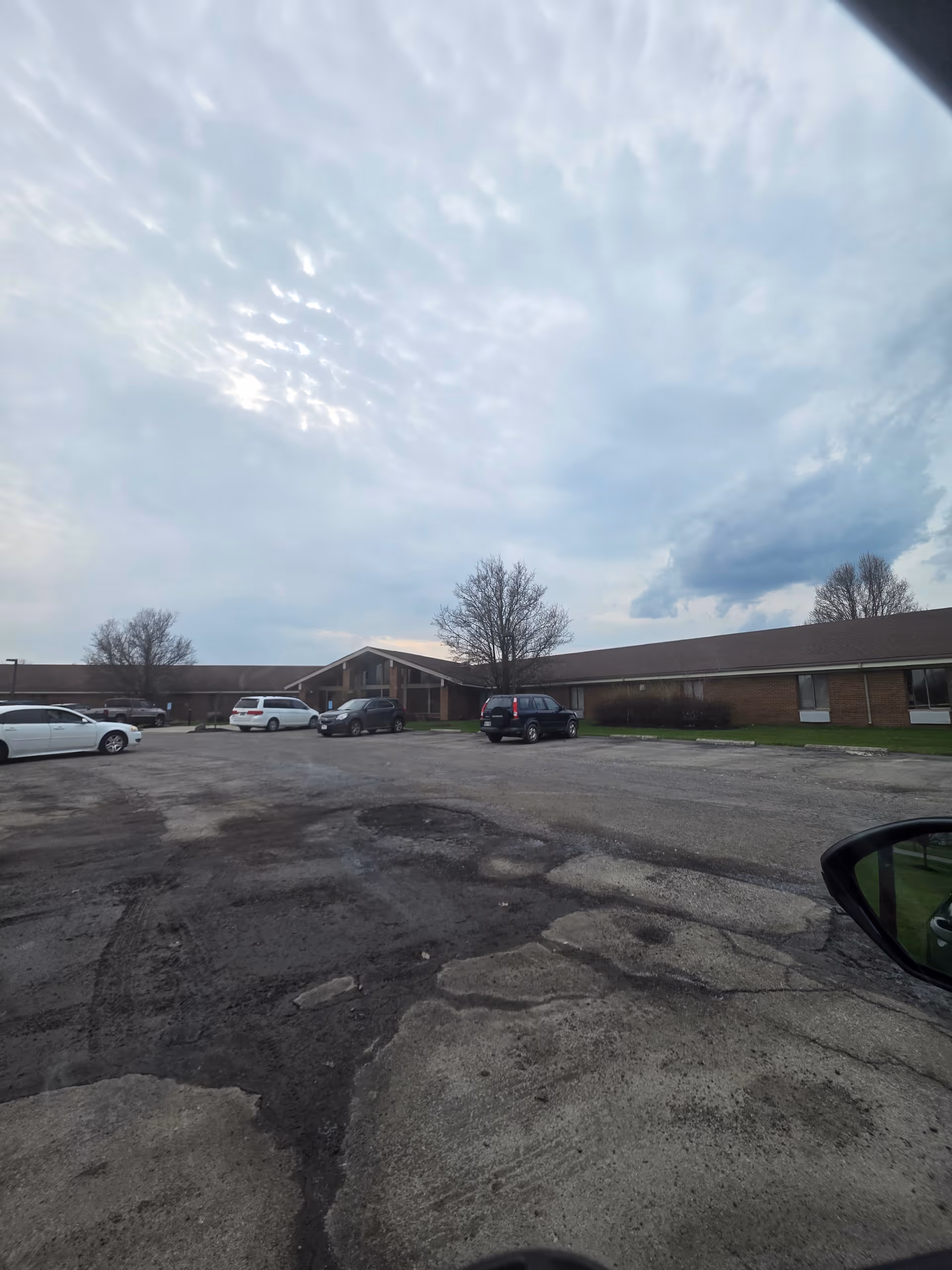 Exterior view of a single-story brick senior living facility with cars in the parking lot.