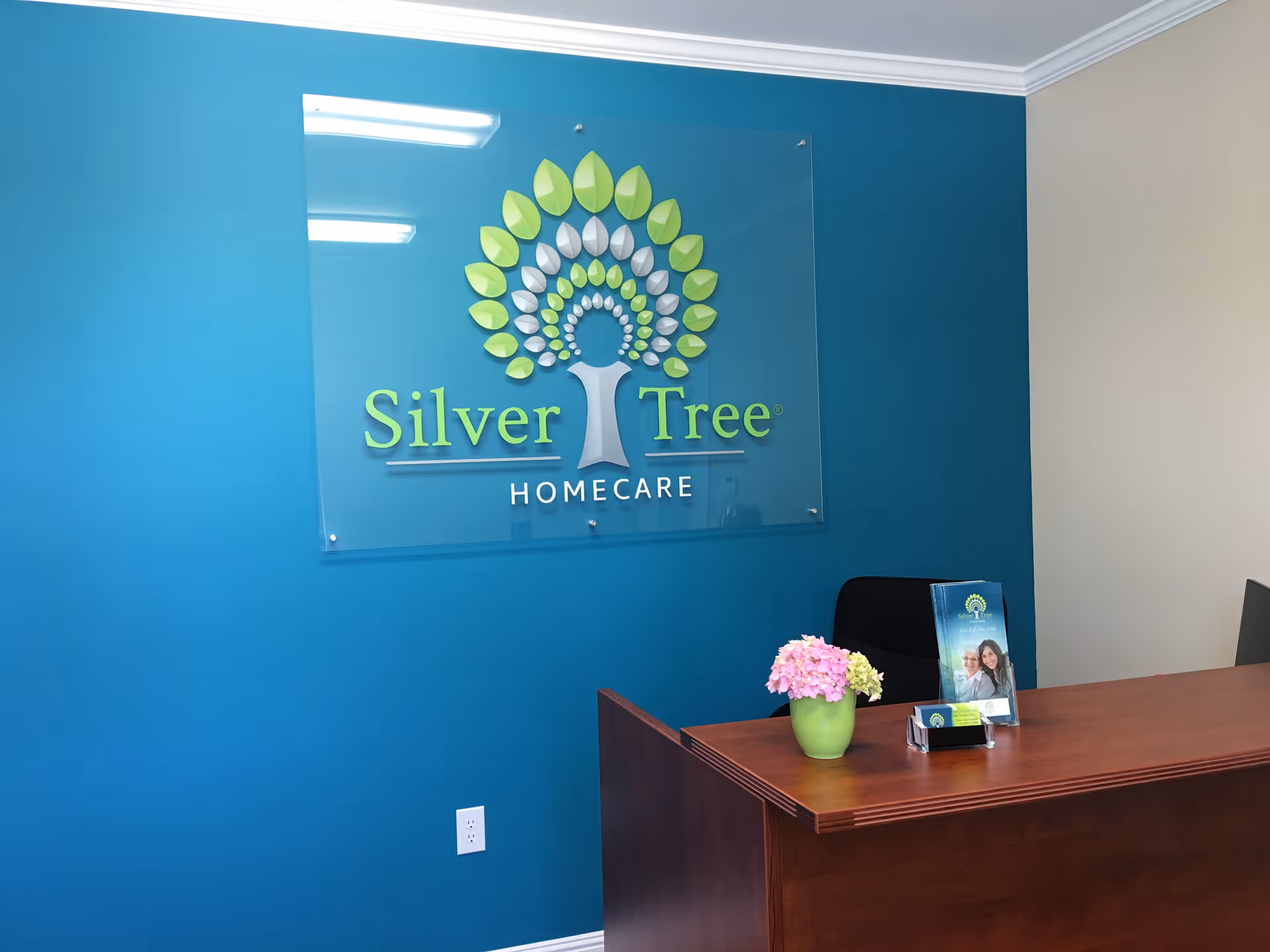 Blue-walled reception area featuring Silver Tree HomeCare sign and a desk plant.
