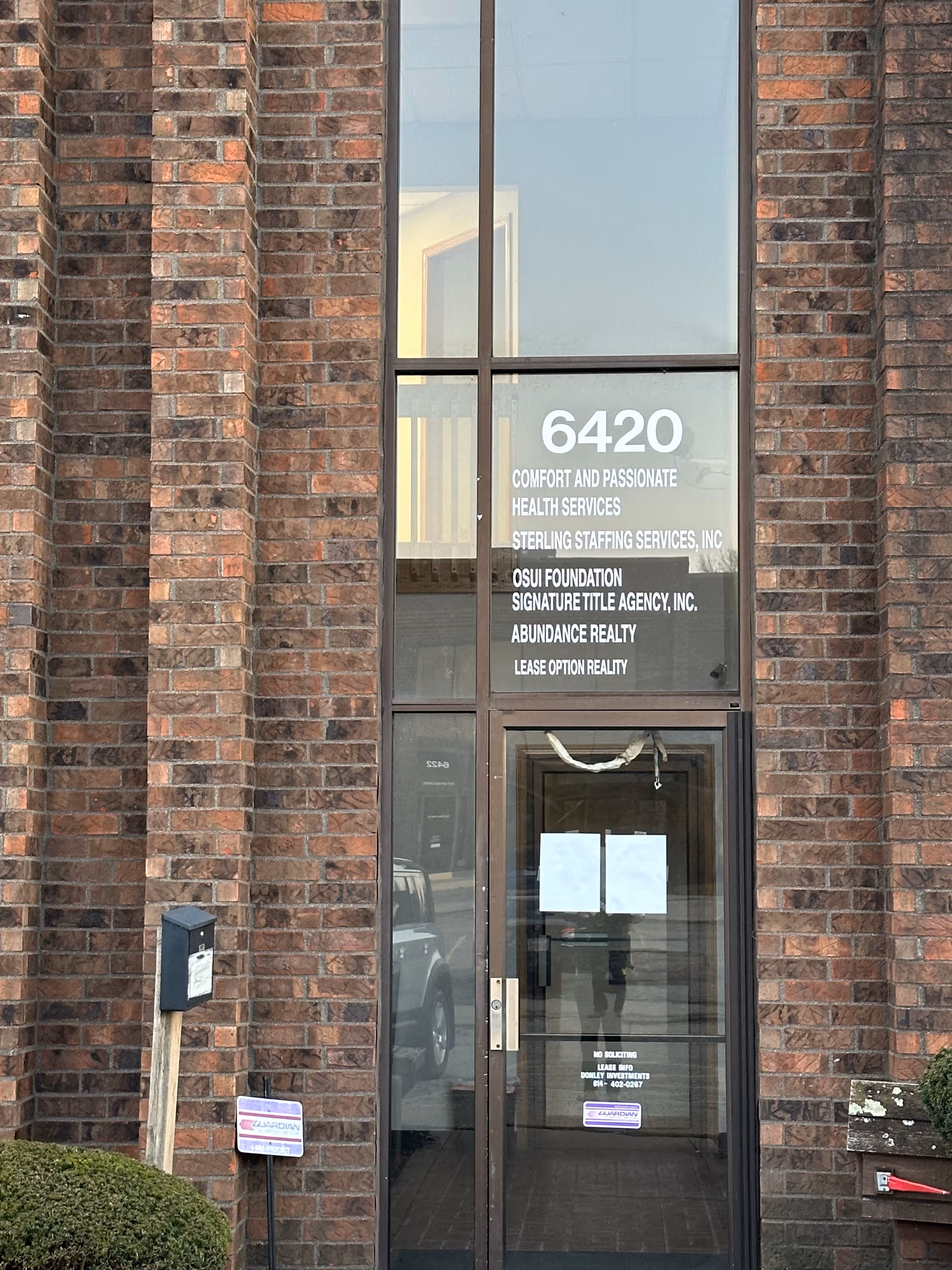 Brick building facade with glass front door displaying address 6420 and service names.