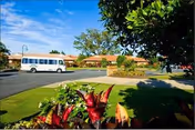 The Meadows at Cypress Gardens exterior with a parked bus, landscaped lawn, and sunny sky.