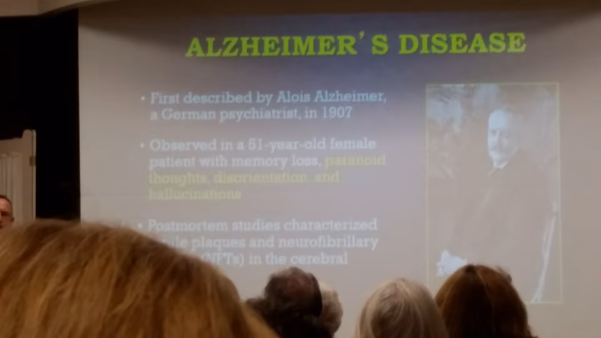 Projection slide about Alzheimer's disease with audience members visible in the foreground.