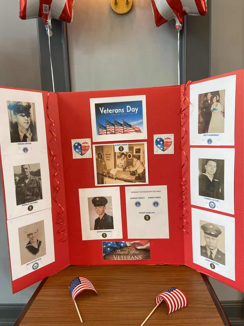 Red tri-fold display board with Veterans Day photos and American flags.