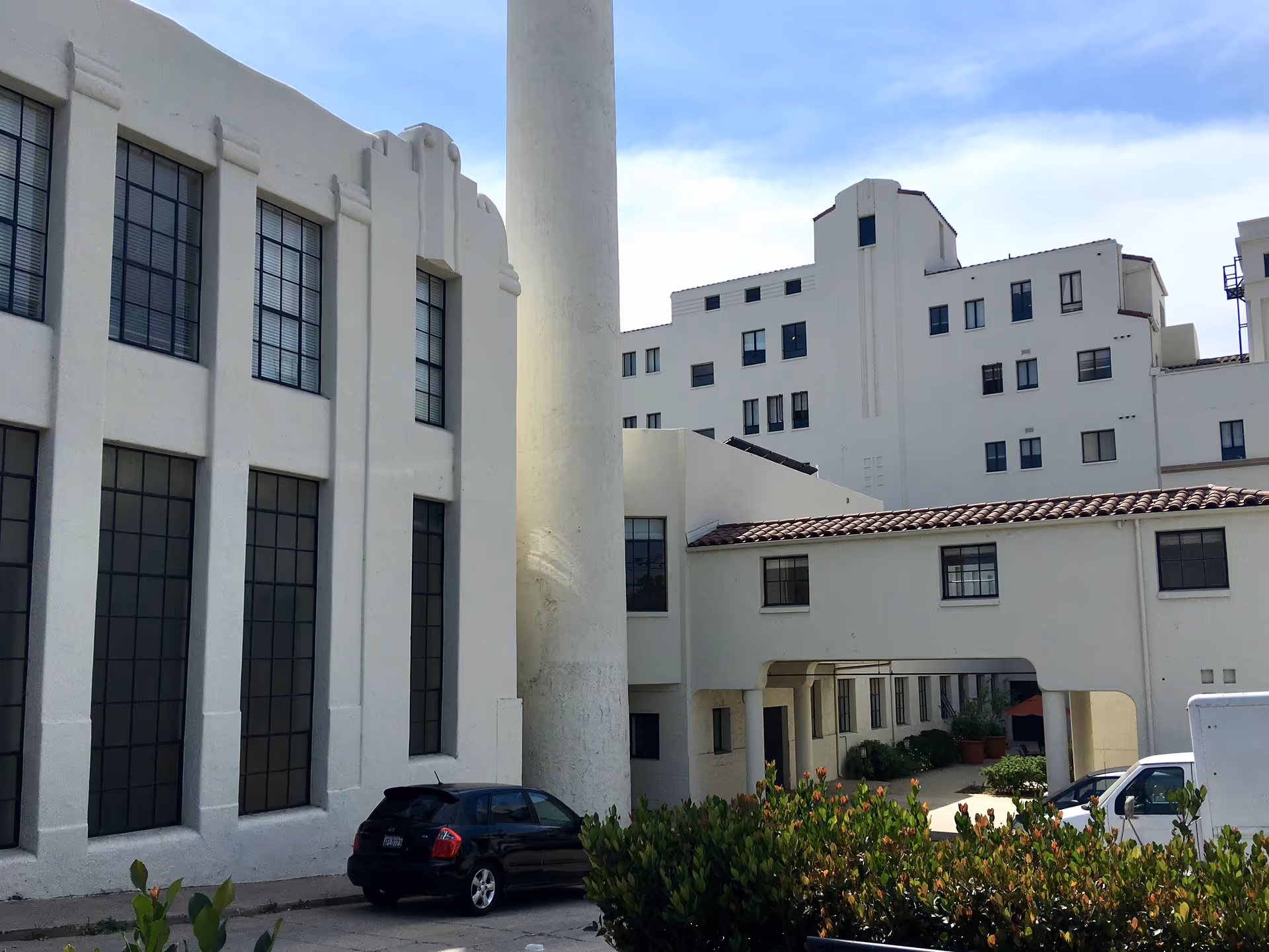 White exterior of Hollenbeck Terrace senior living with tall windows, parked cars, and shrubs.