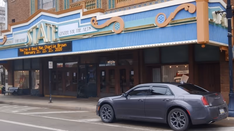 The theater building with a blue marquee and a gray car parked outside.