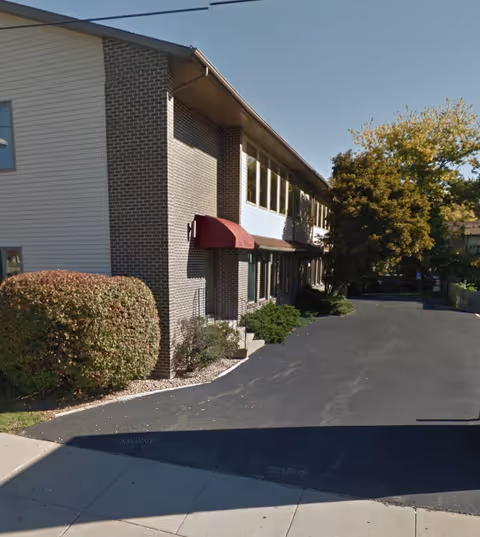 Exterior view of a two-story senior care facility with brick, siding, and red awning.