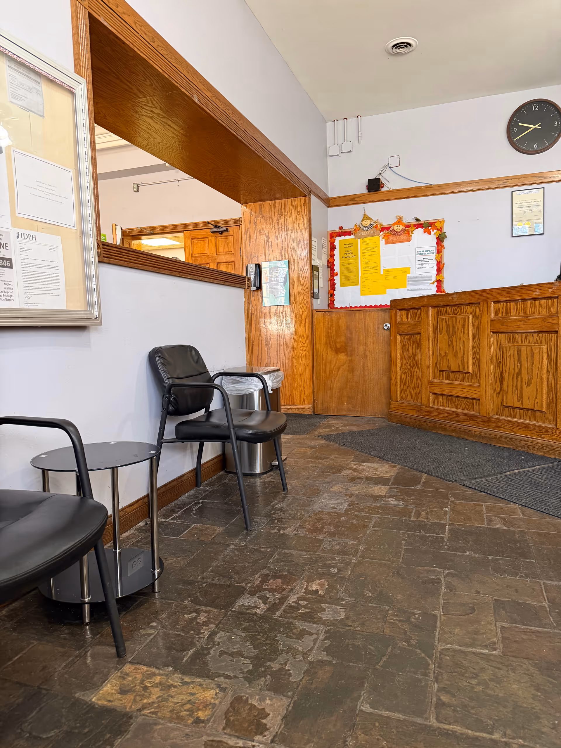 Lobby area with black chairs, bulletin boards, wooden paneling, and a clock on the wall.