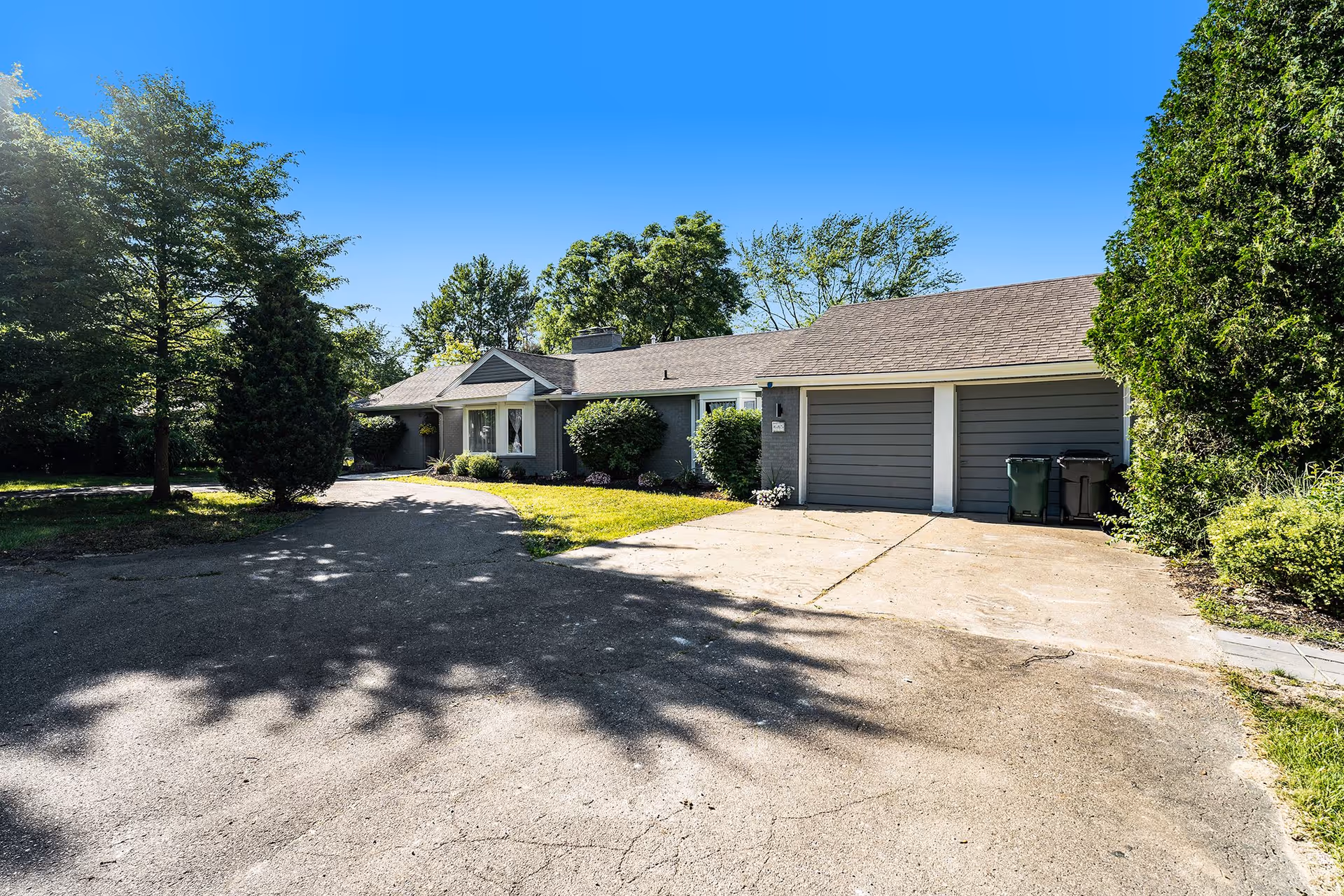 Front view of a single-story residential building with three garage doors and surrounding trees.