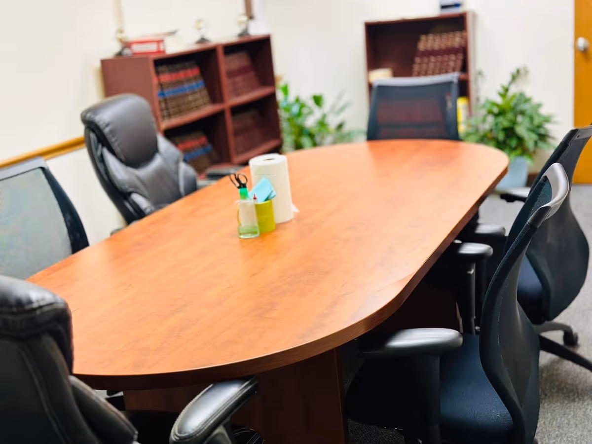 Oval wooden conference table with chairs, supplies, shelves, and plants in a meeting room.