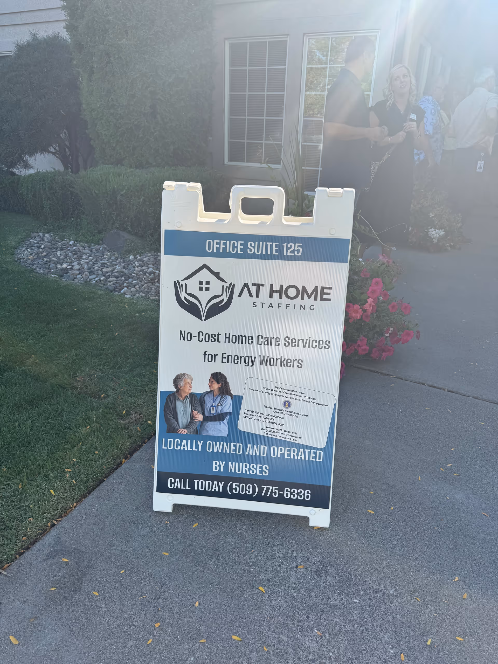 Outdoor A-frame sign for At Home Staffing outside a facility entrance with people nearby