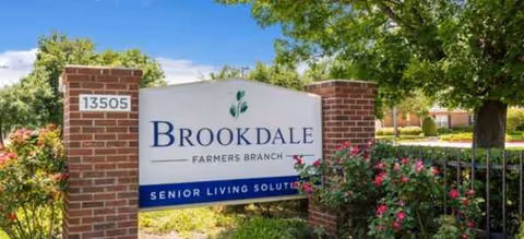 Brookdale Farmers Branch entrance sign between brick pillars with blooming shrubs