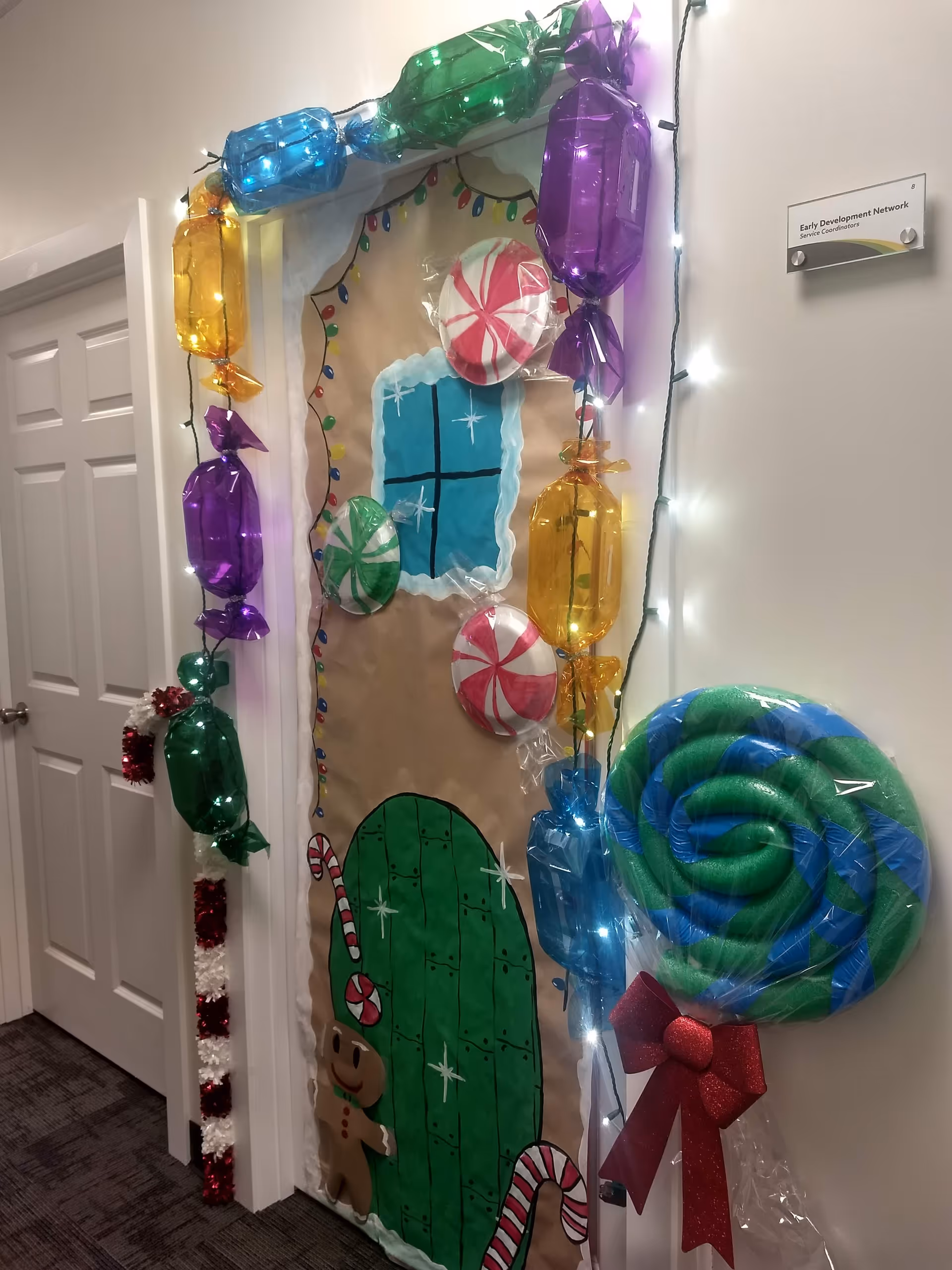 A festive hallway doorway in a senior living facility decorated with candy props and lights.