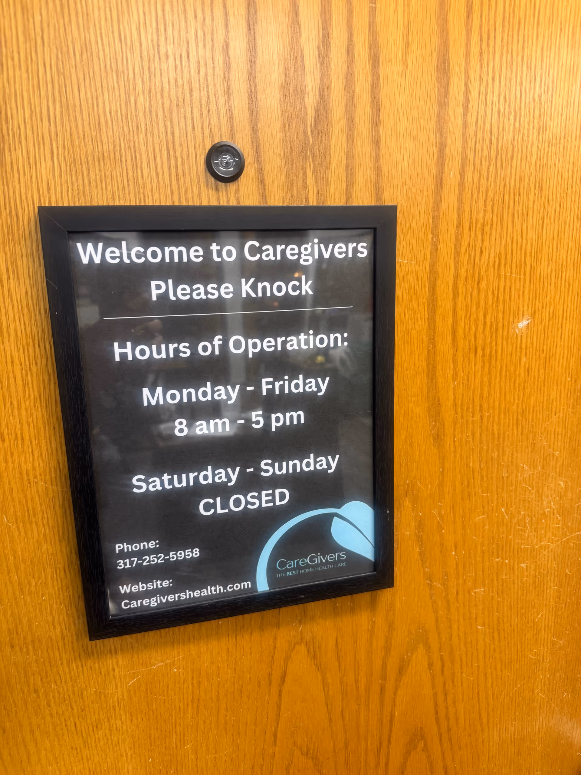 Wooden door with a framed sign displaying Caregivers' hours and contact information.