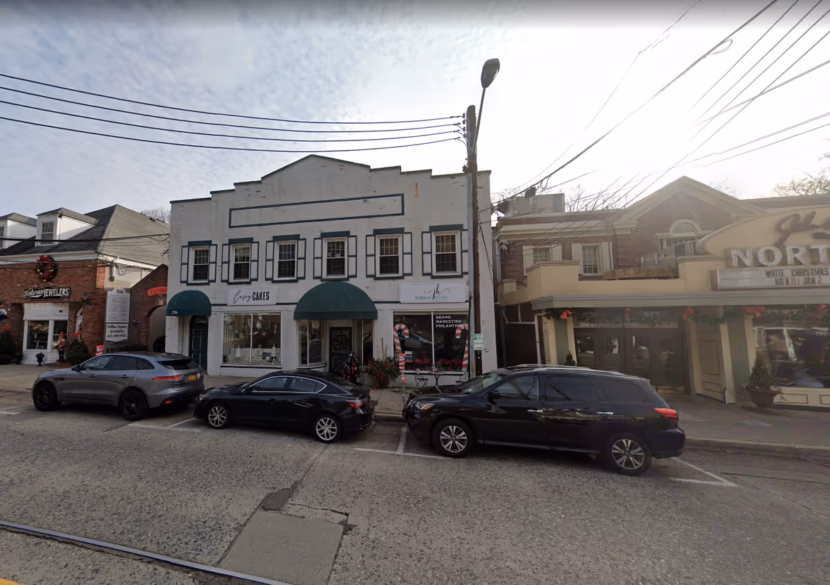A street scene with small storefronts and parked cars along the road.