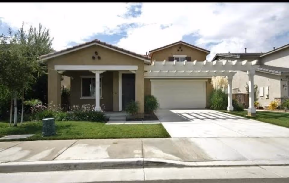 Single-story beige home with a white pergola and attached garage.