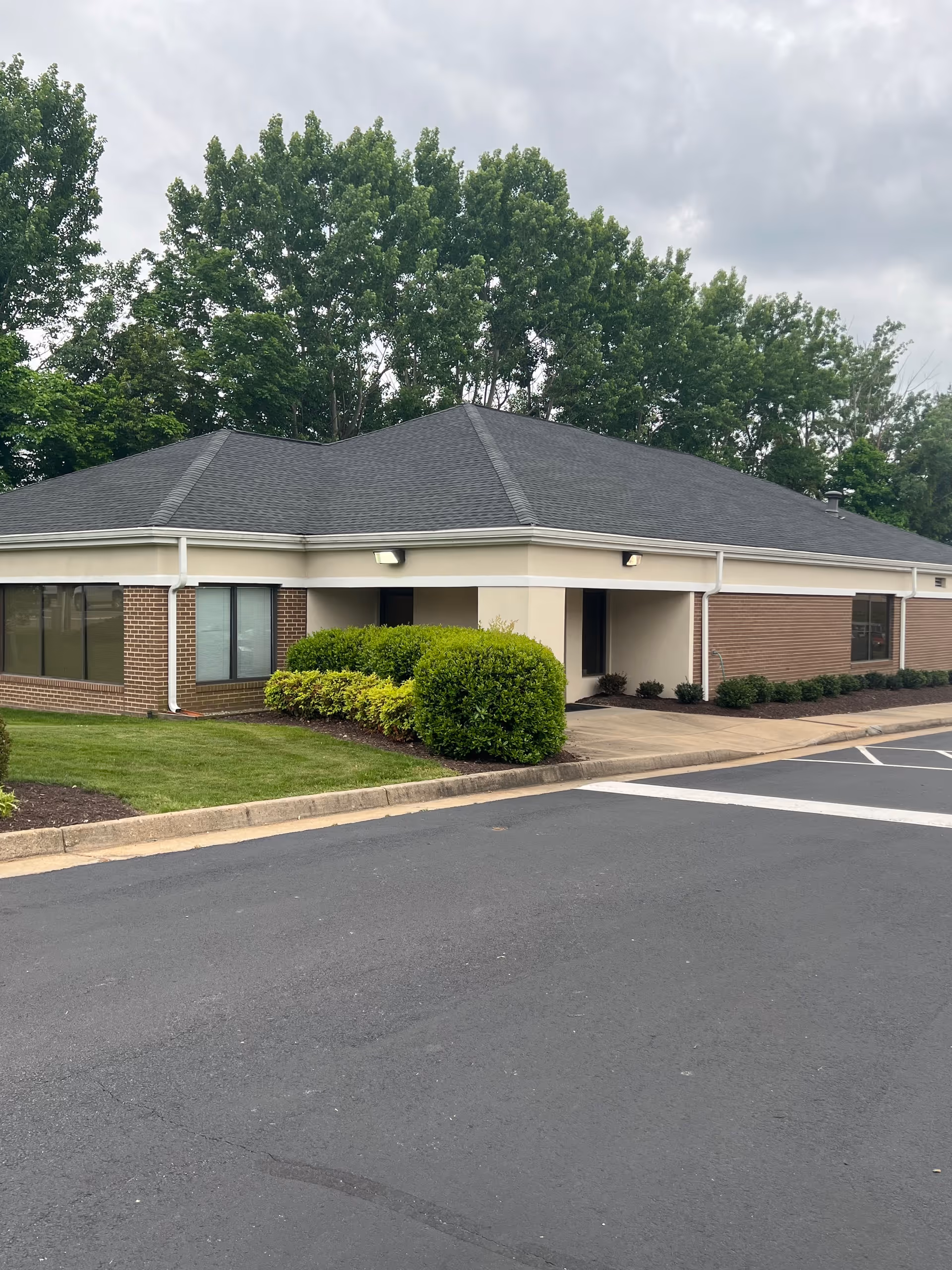 Single-story senior living facility exterior with entrance, parking, and trimmed shrubs.