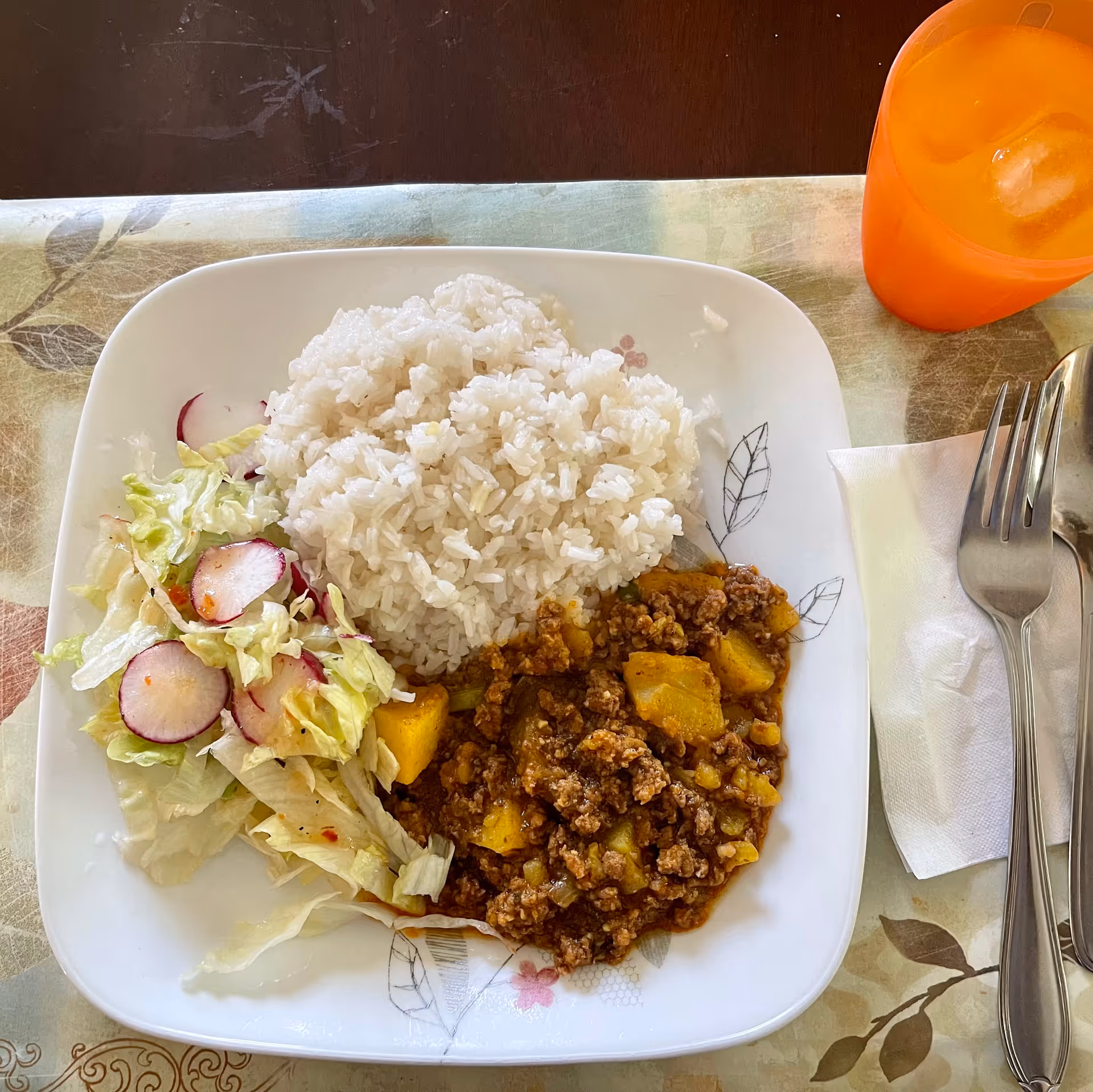 Plate of rice, ground beef with potatoes, and salad on a dining table.