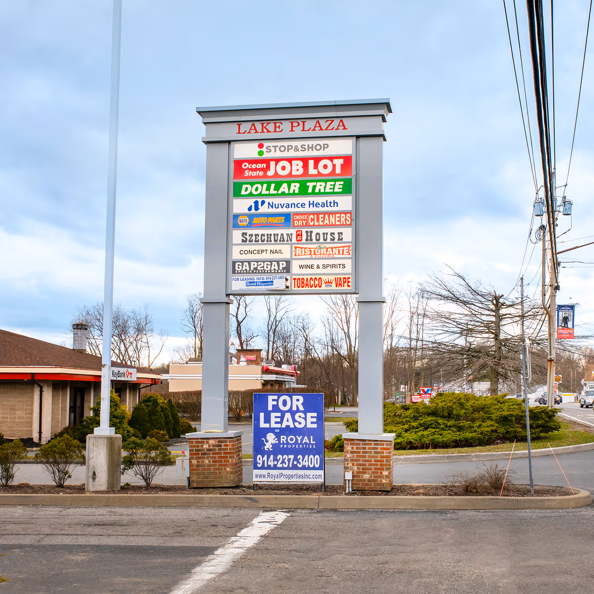 A tall signboard displays multiple shop signs at Lake Plaza with a blue For Lease sign.