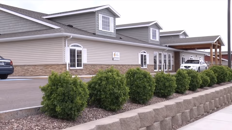 Exterior view of BeeHive Homes of Great Falls with shrubs and parked cars.