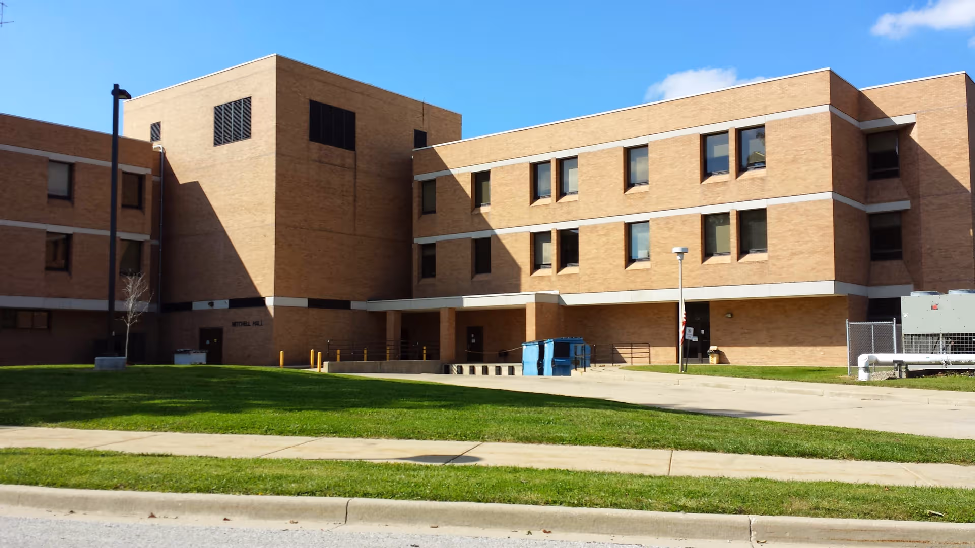 Brick senior living facility exterior with a manicured lawn and clear blue sky.