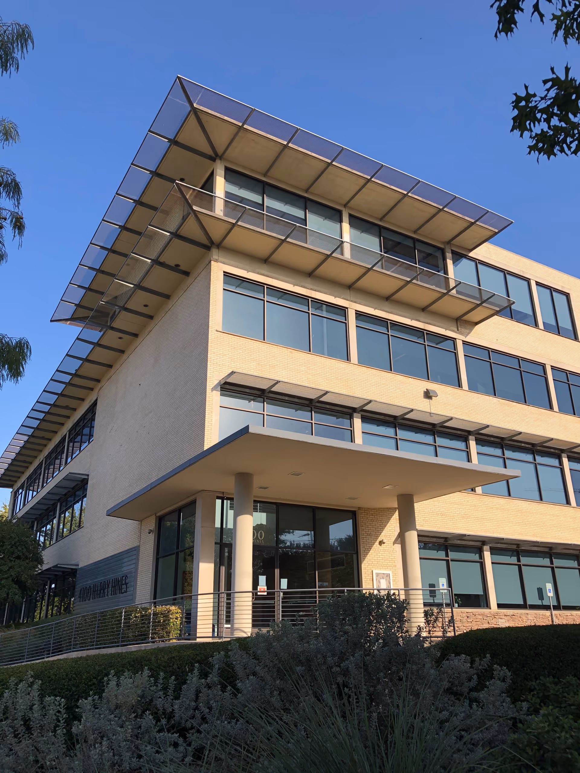 Modern multi-story building with glass windows, a covered entrance, and landscaped surroundings.